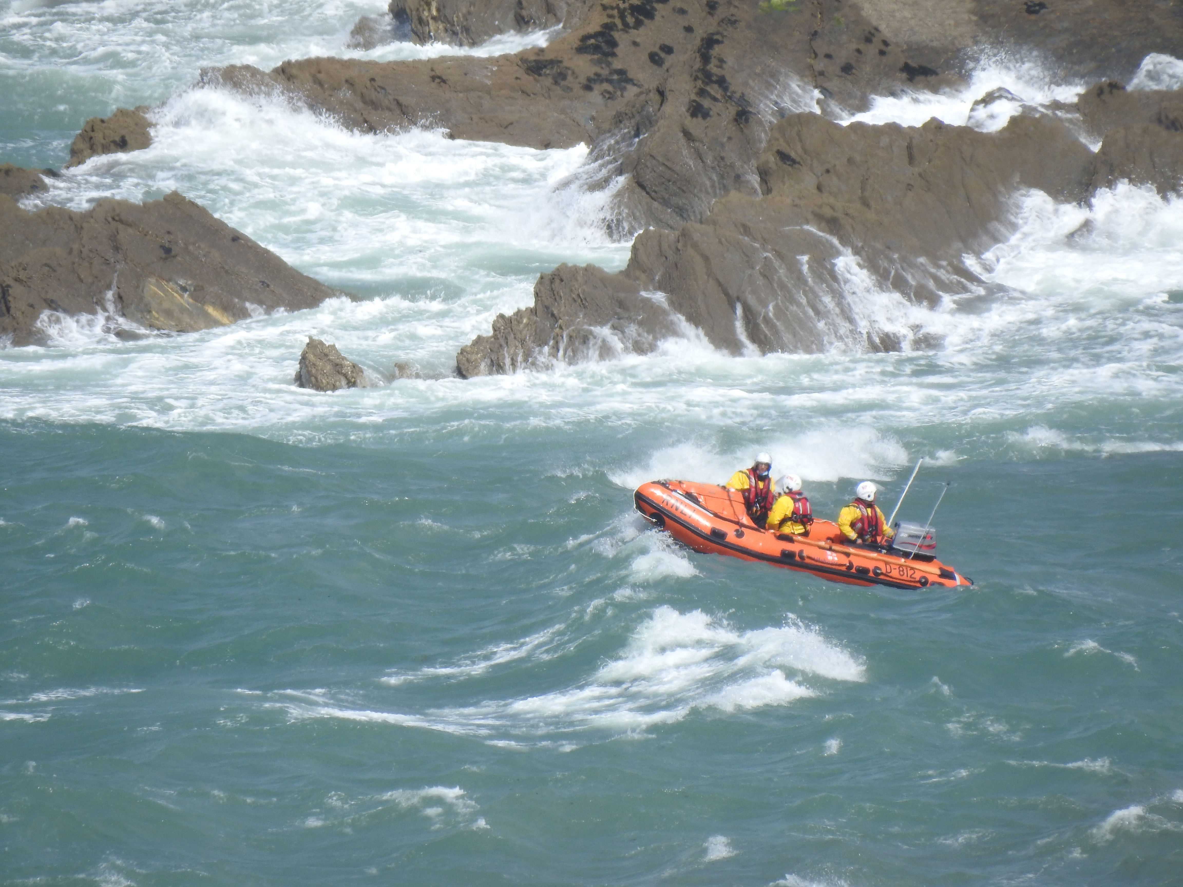 Inshore lifeboat near rocks in large swell with breaking waves