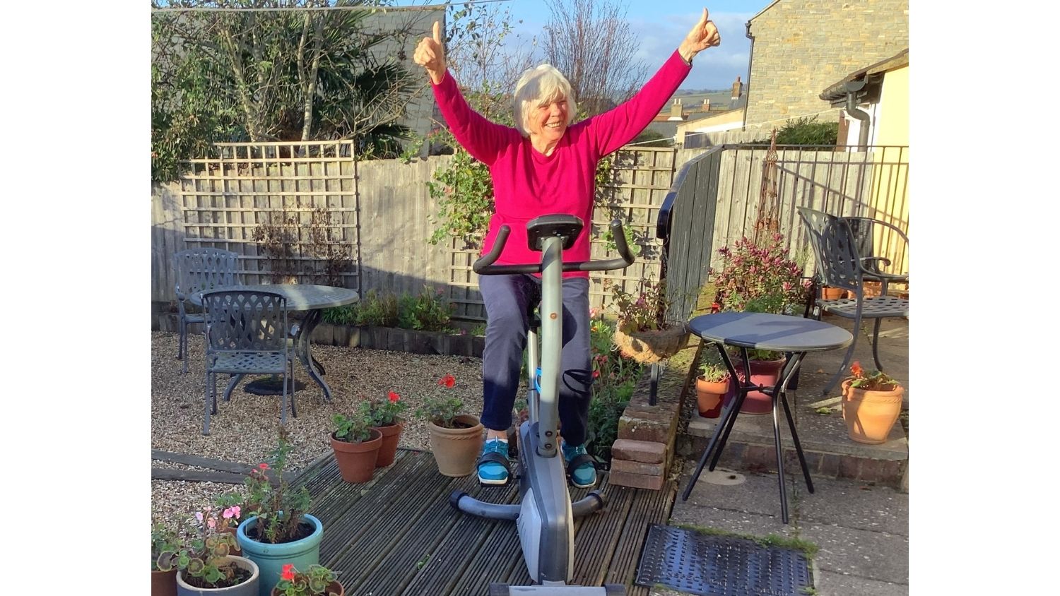 A woman sits on an exercise bike raising her hands in the air in celebration