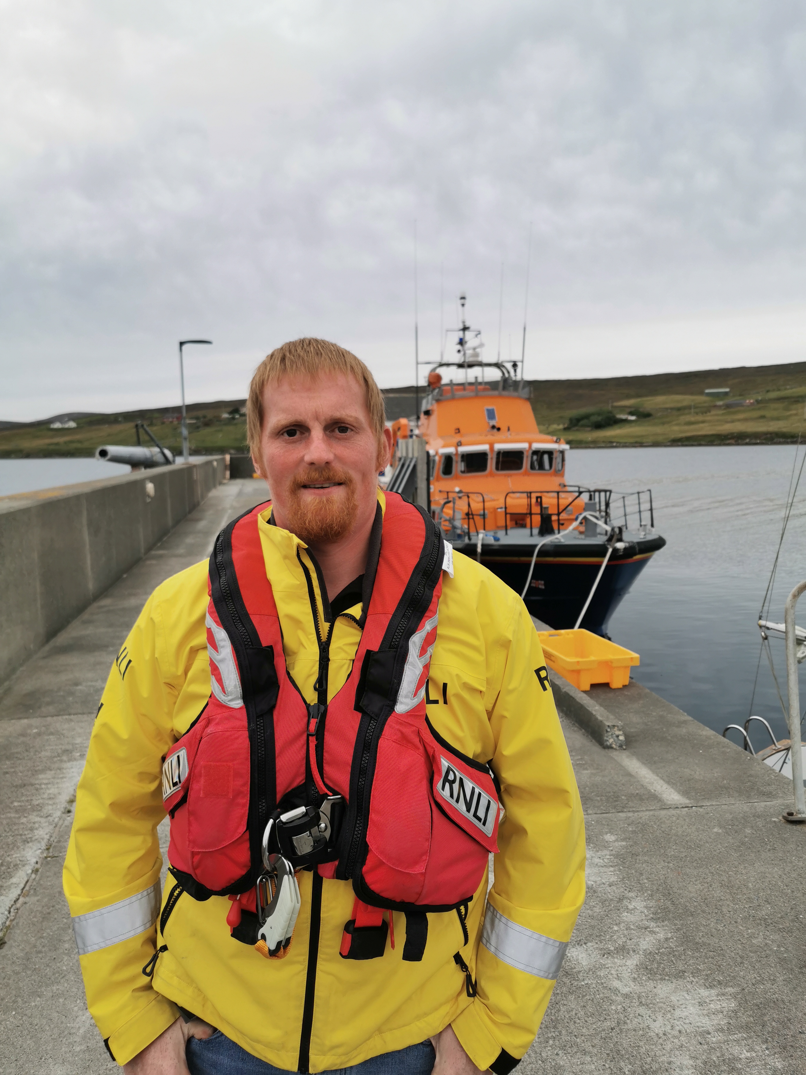 Portrait of Steven in RNLI jacket and life vest standing in front of RNLI lifeboat