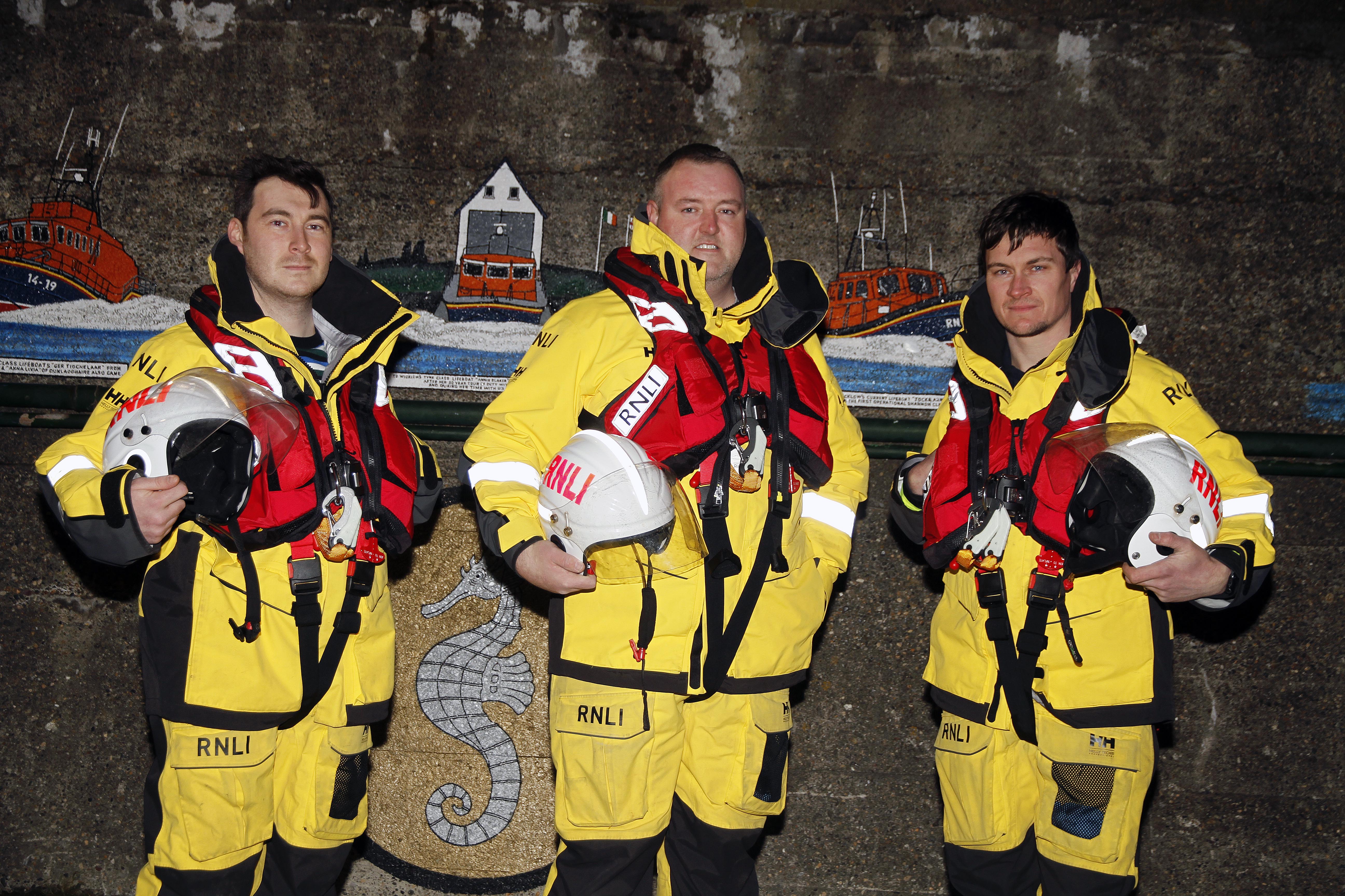 Three crew members in full kit in front of a wall with a mural of lifeboats