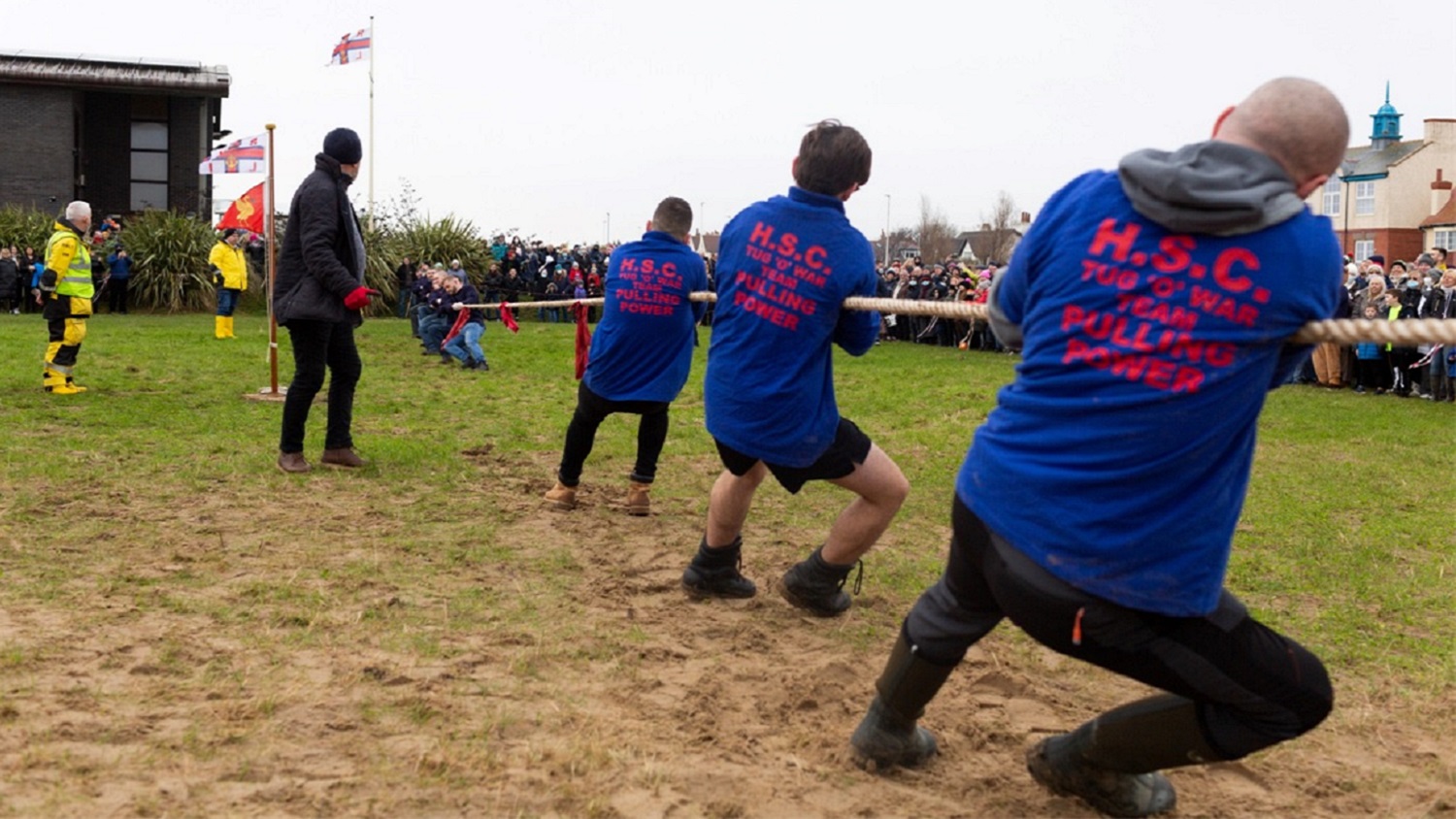 Men pull at a tug of war rope in a green field.