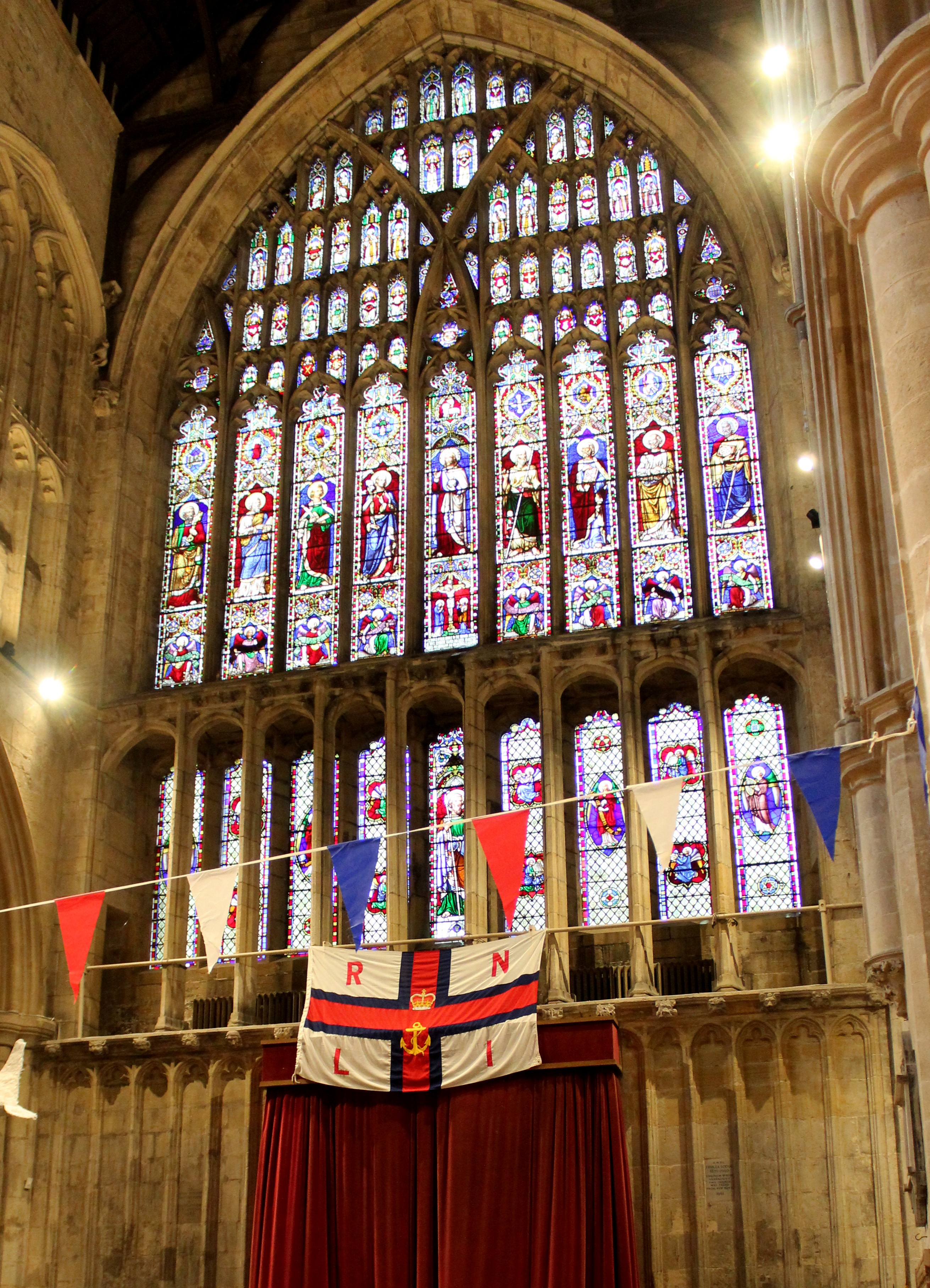 An RNLI flag hangs in front of a stained glass window in a church