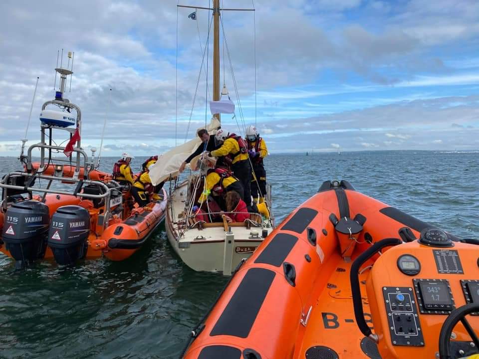 Cowes lifeboat in the foreground, with Calshot lifeboat alongside the yacht and lifeboat members aboard it to provide assistance.