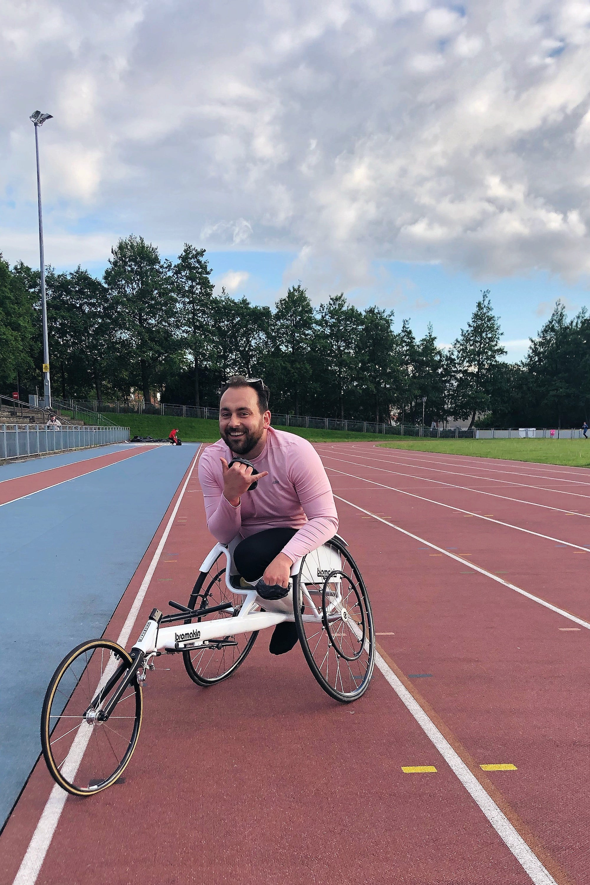 A man in a pink shirt sits in a bicycle wheelchair on an athletics track.