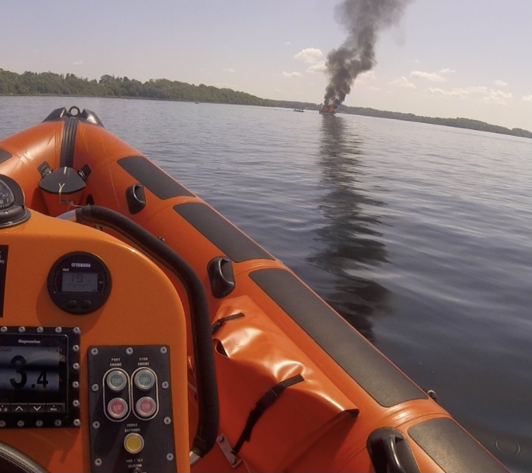 Over the bow of the lifeboat, the casualty vessel on fire