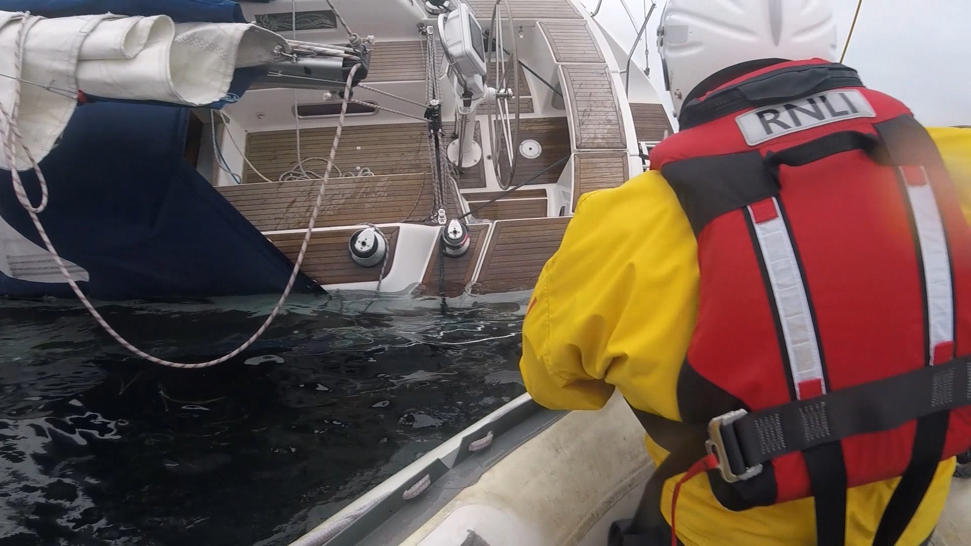 two lifeboat crew approach a stricken yacht on it's port side.