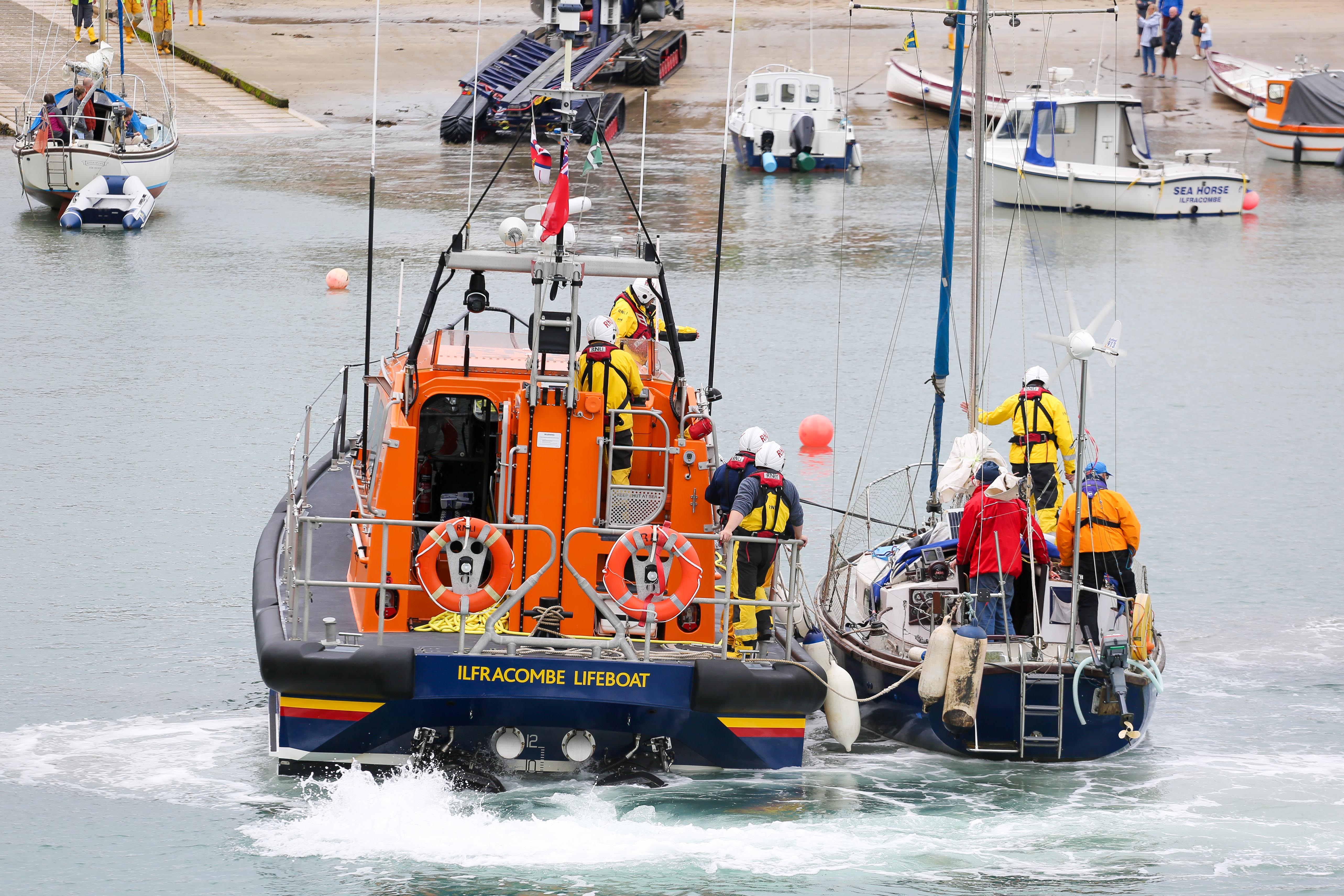 Small yacht towed alongside lifeboat being placed on mooring