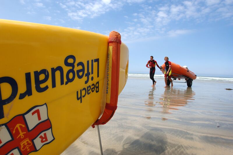 Yellow RNLI rescue board with two lifeguards carrying a boat in the background