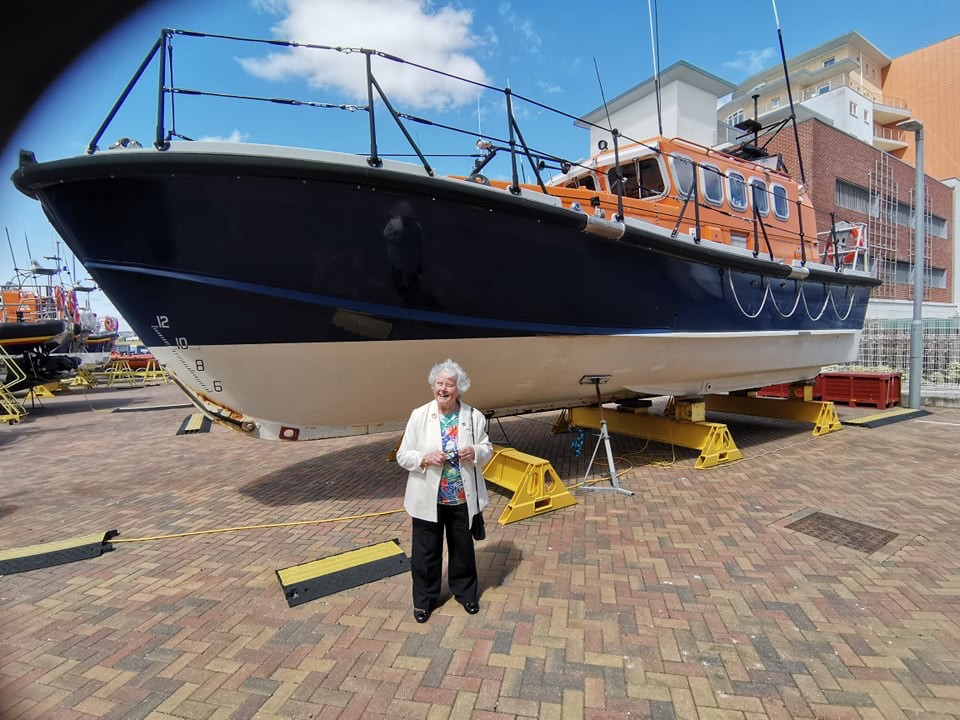 A lady stands in front of an older lifeboat 