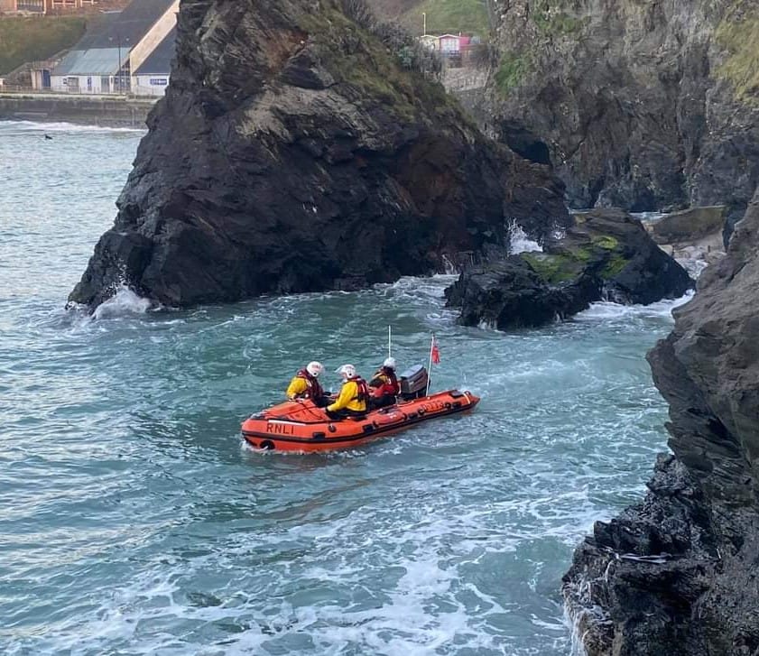 RNLI crew in D class inshore lifeboat pull away from rocks with two boys safely onboard