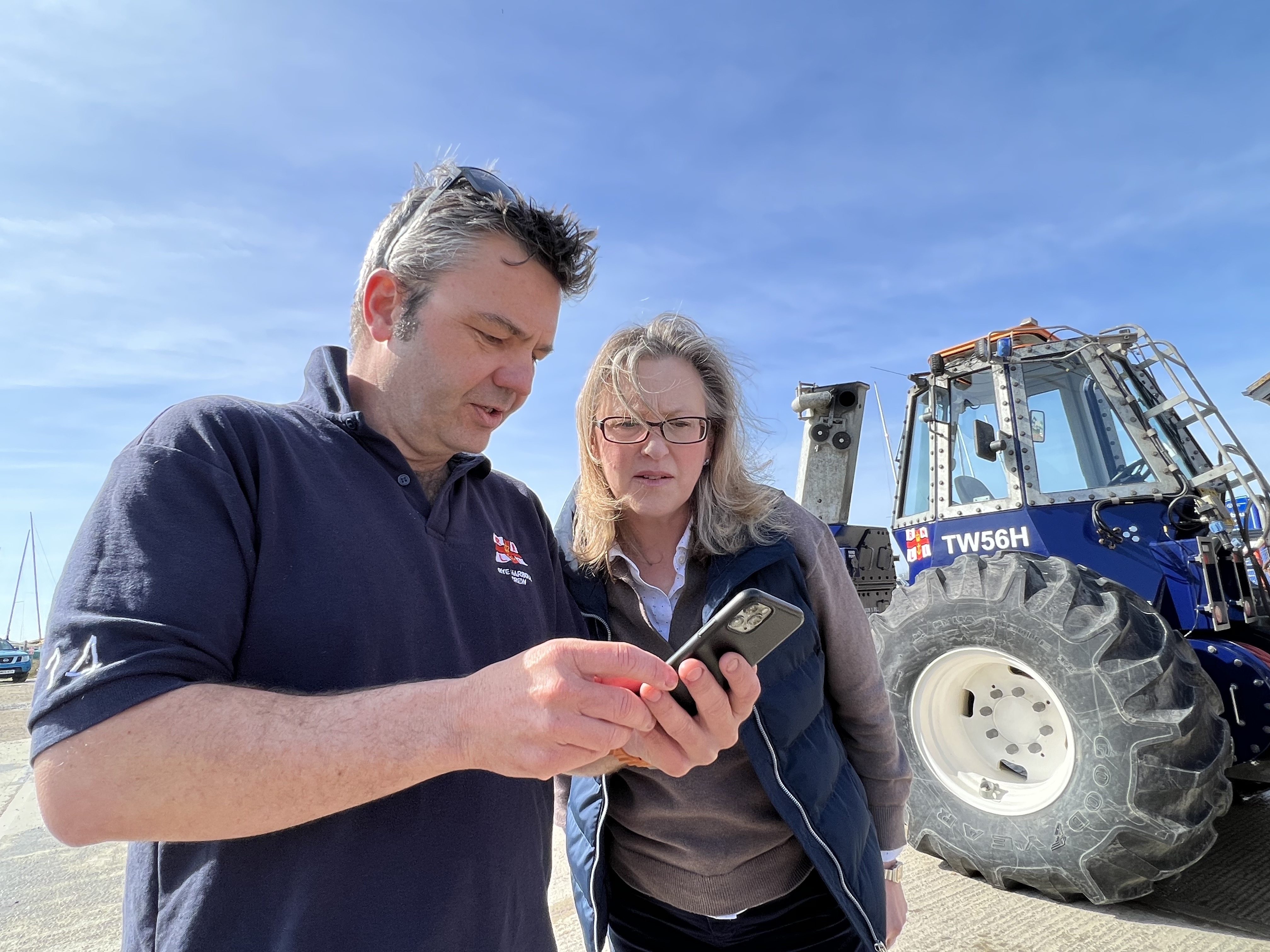 A crew member shares a video on his mobile phone with Sall-Ann Hart in front of the tractor