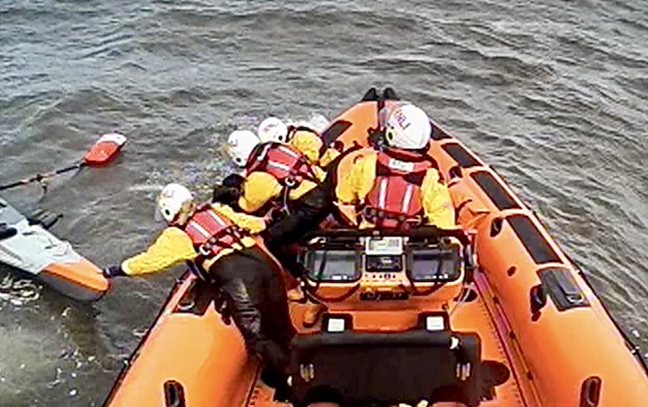 The Queensferry RNLI lifeboat is on scene, two volunteer crew are bringing the casualty on board, one volunteer crew is managing the kayak, one crew member is helming the lifeboat.