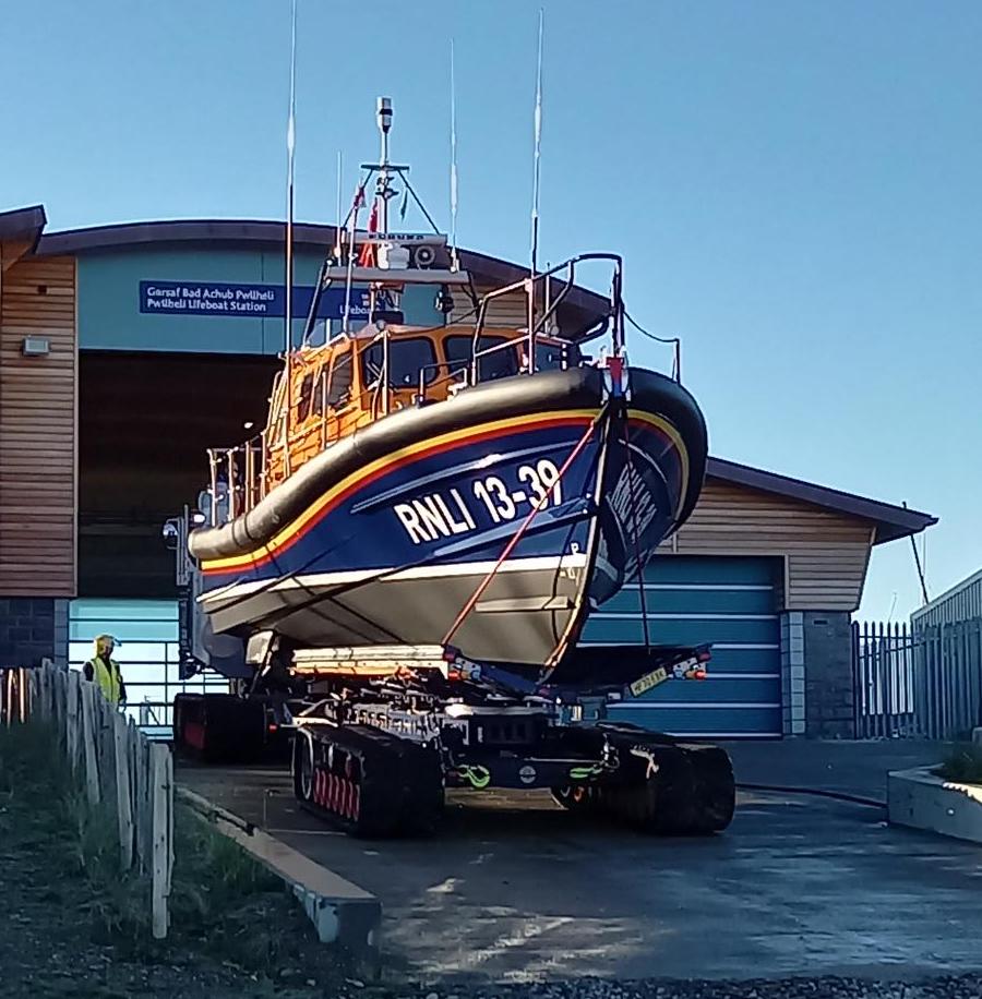Pwllheli RNLI all-weather Shannon lifeboat on its carriage on the slipway in front of the boathouse in the daytime with a blue sky