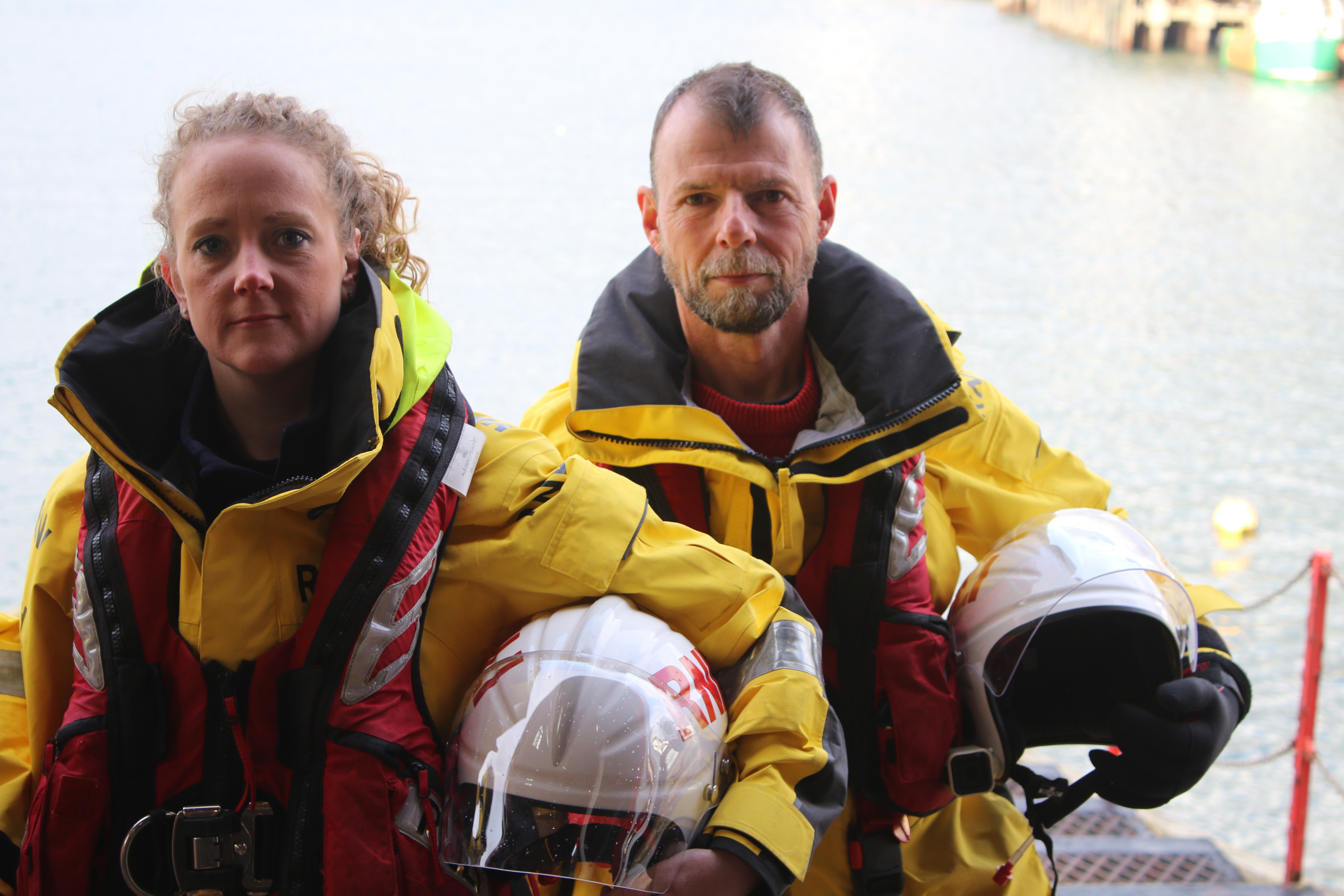 One man and one woman holding helmets in front of the sea
