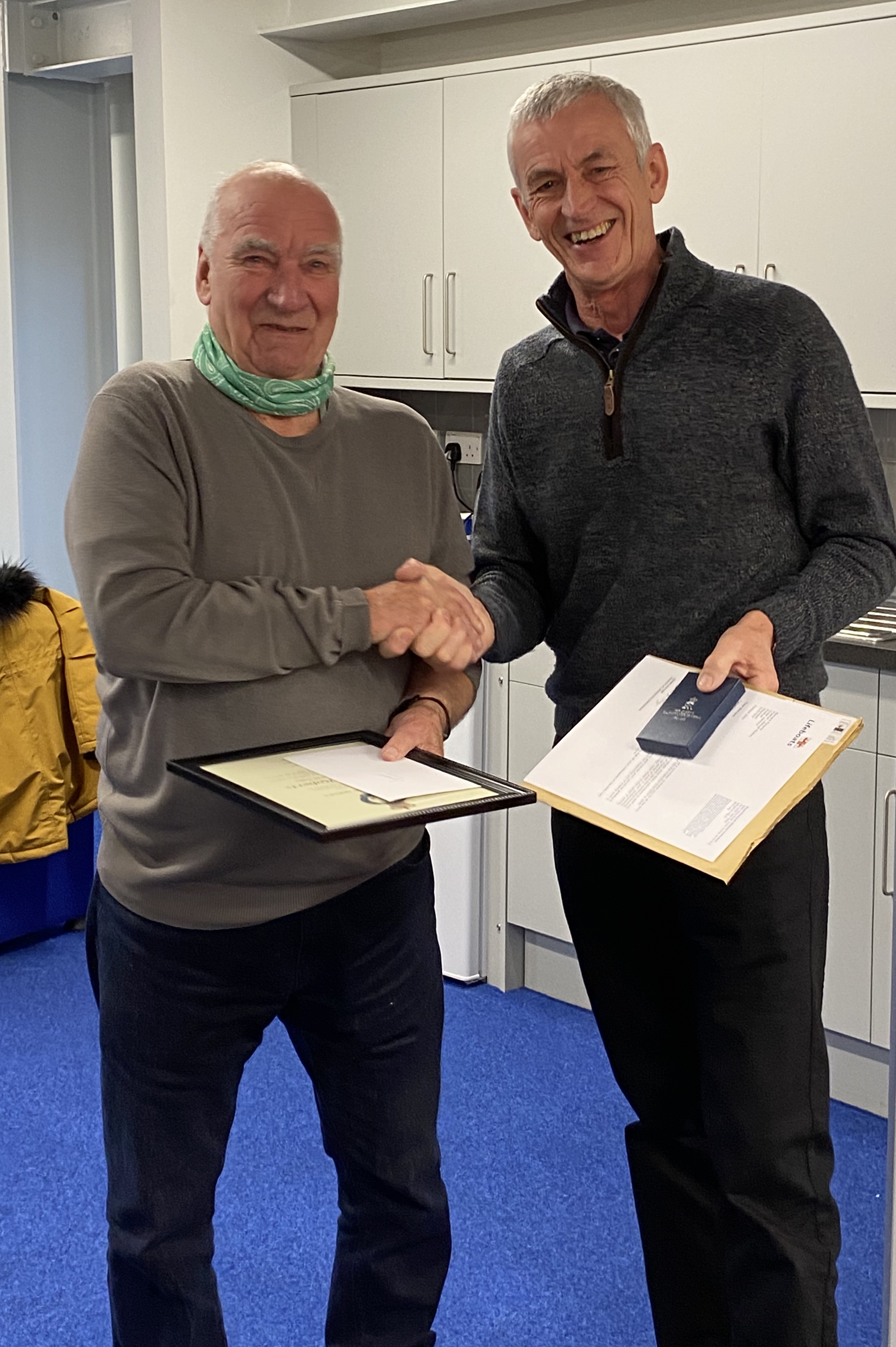 Bernard Roberts standing on the left of the photo is shaking hands with Pwllheli RNLI Lifeboat Operations Manager Andy Vowell has he receives his letter of thanks and Queen's Jubilee Medal