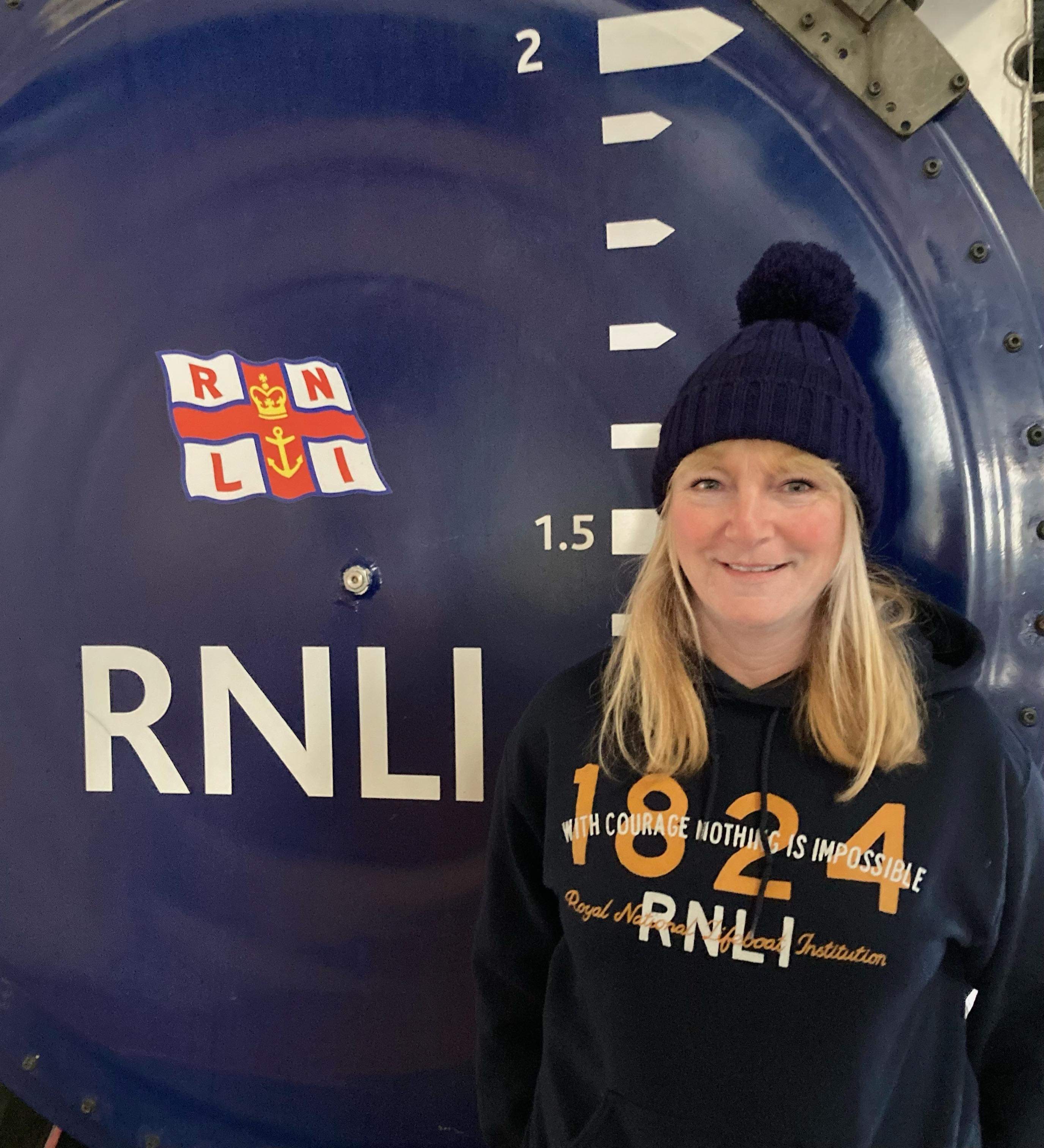 A lady in a hat with long blonde hair stands in front of the tractor with RNLI logo