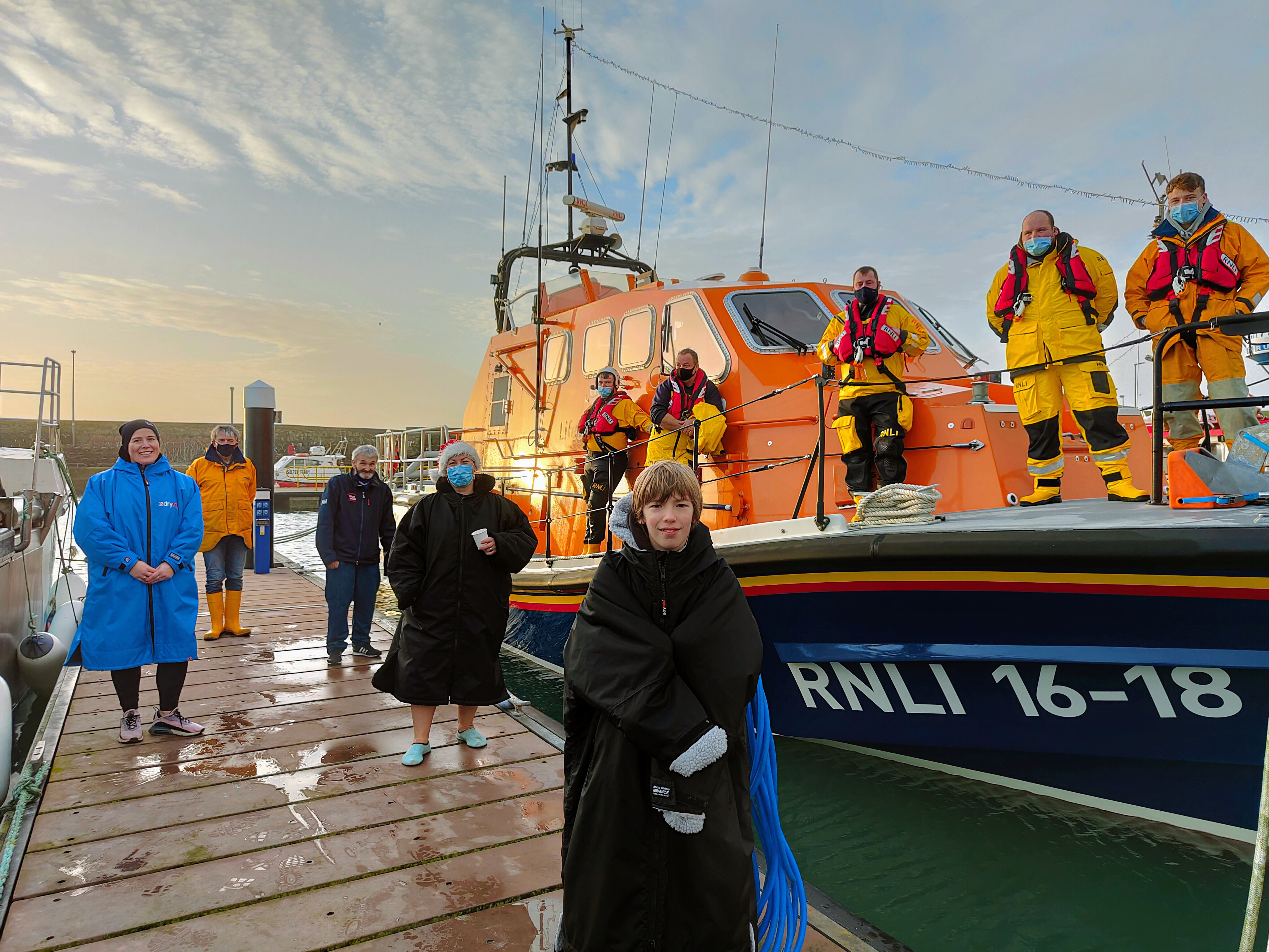 The attached photo shows Kilmore Quay RNLI crew onboard the RNLB Killarney in Kilmore Quay marina, with Grainne O'Brien (20 Dips in December Organizer), John Grace (Lifeboat Operations Manager), Johnny Moore (Chair of the Kilmore Quay RNLI Fundraising Committee, Melinda Kehoe (20 Dips in December Organizer), and Tommy Kehoe standing on the marina alongside.