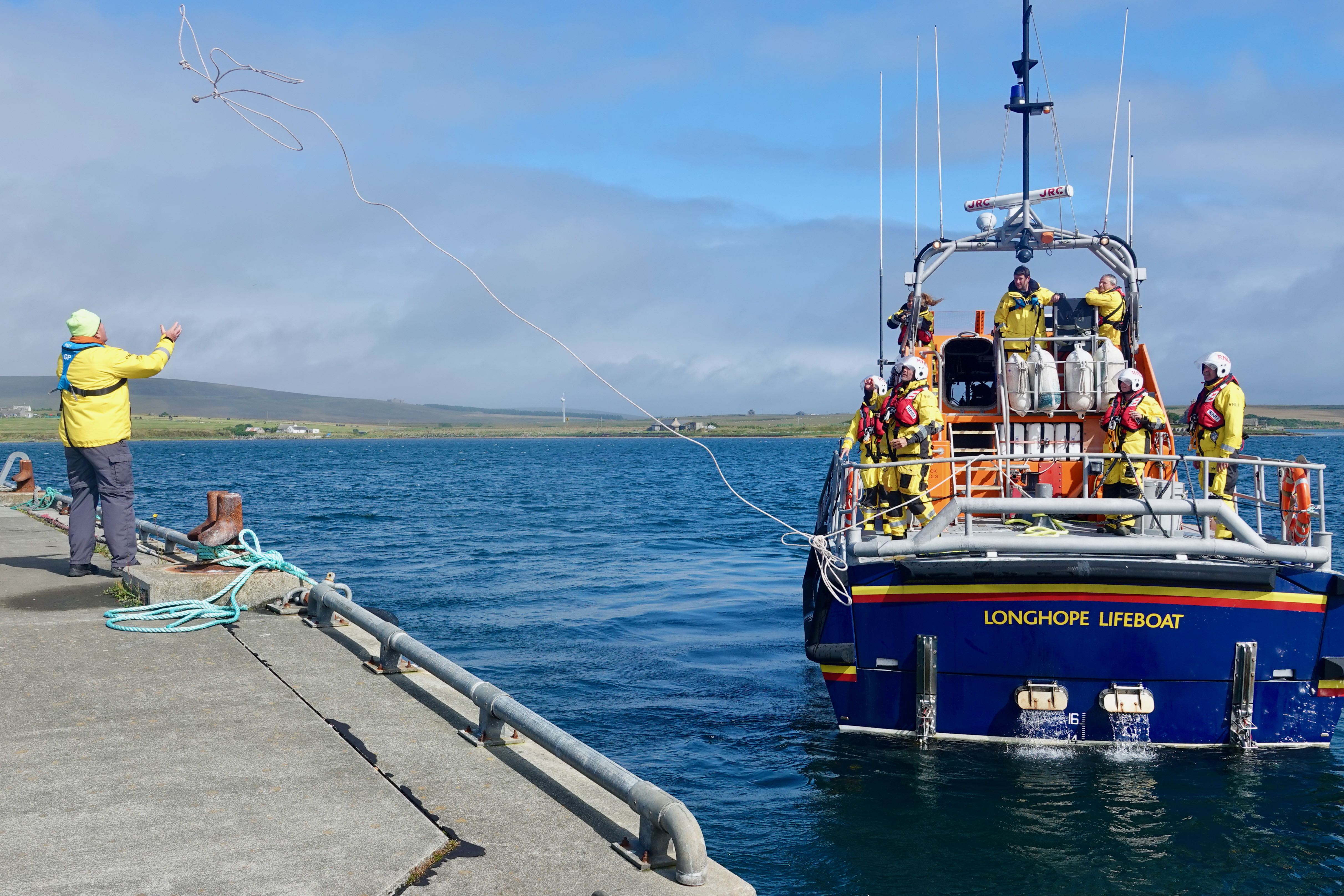 Volunteer crew throw heaving line for tow rope from RNLB Helen Comrie at Longhope Pier
