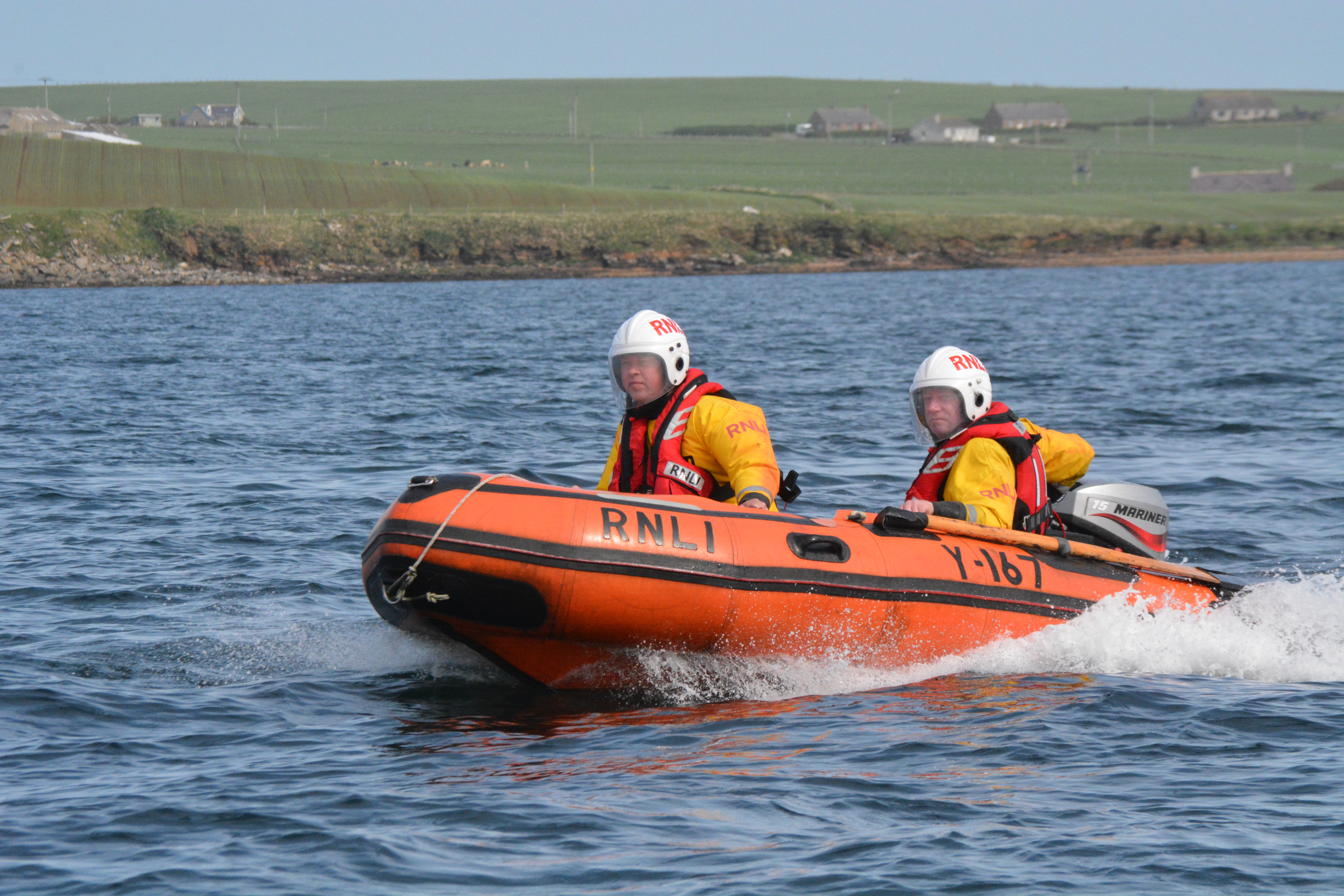 Two crew members wearing helmets speeding along in the Y-boat