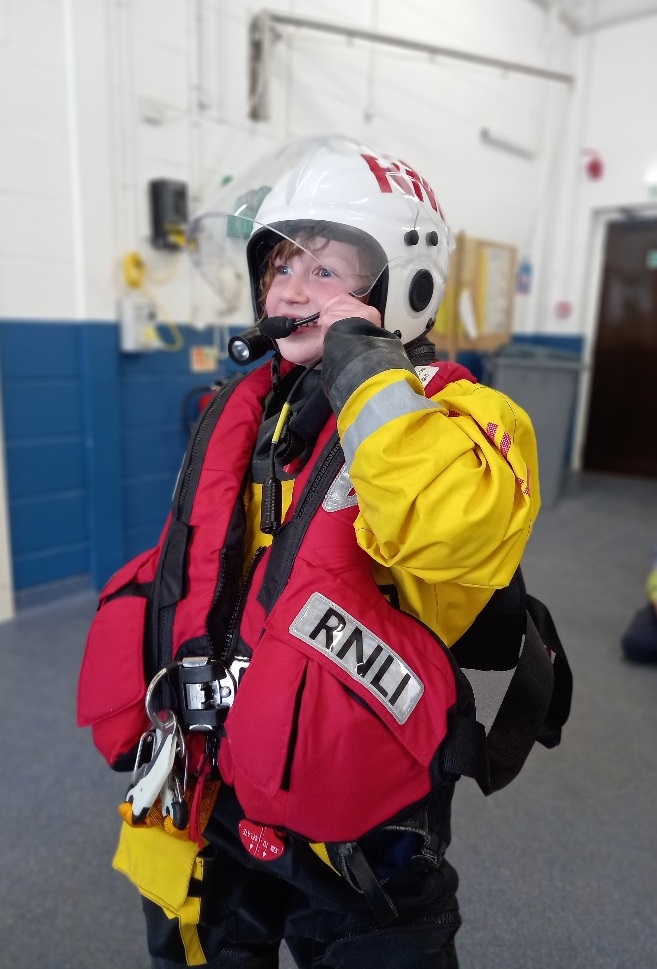 A young school pupil wears the lifeboat crew PPE including lifejacket and helmet