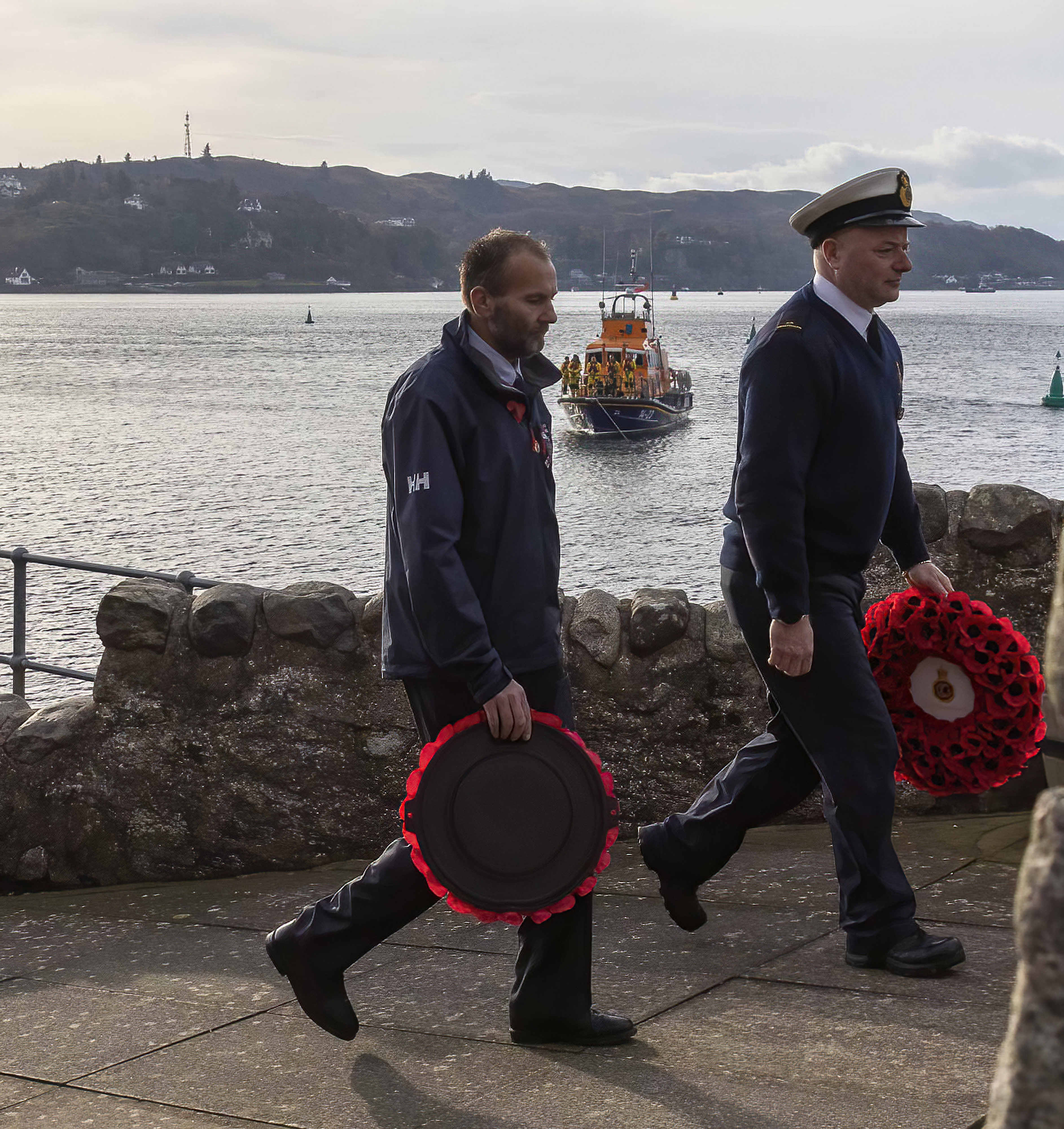 RNLI and Coastguard members lay wreaths with the RNLI lifeboat lying off behind them