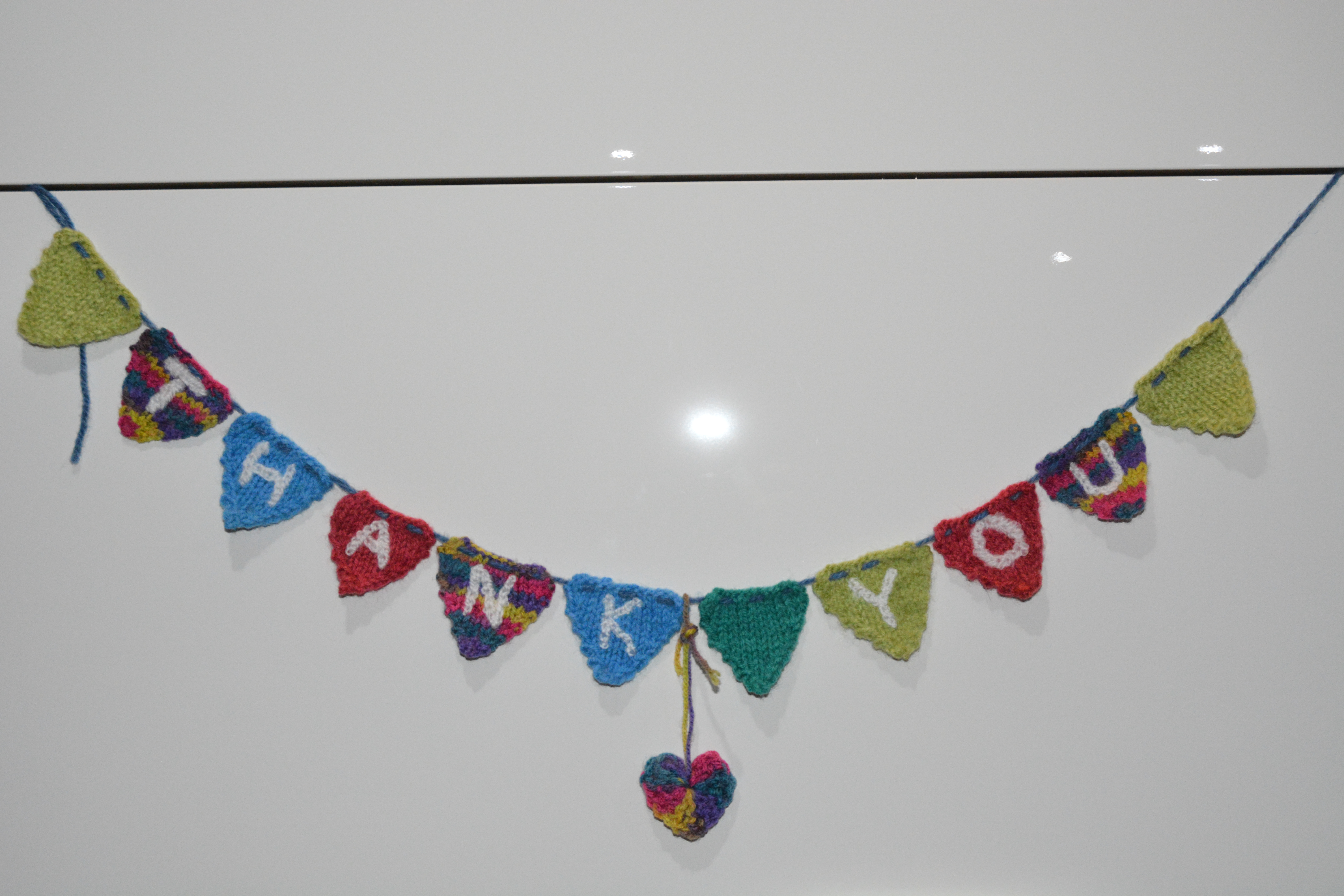 Small, knitted triangles spelling out "Thank You", plus a knitted heart below.