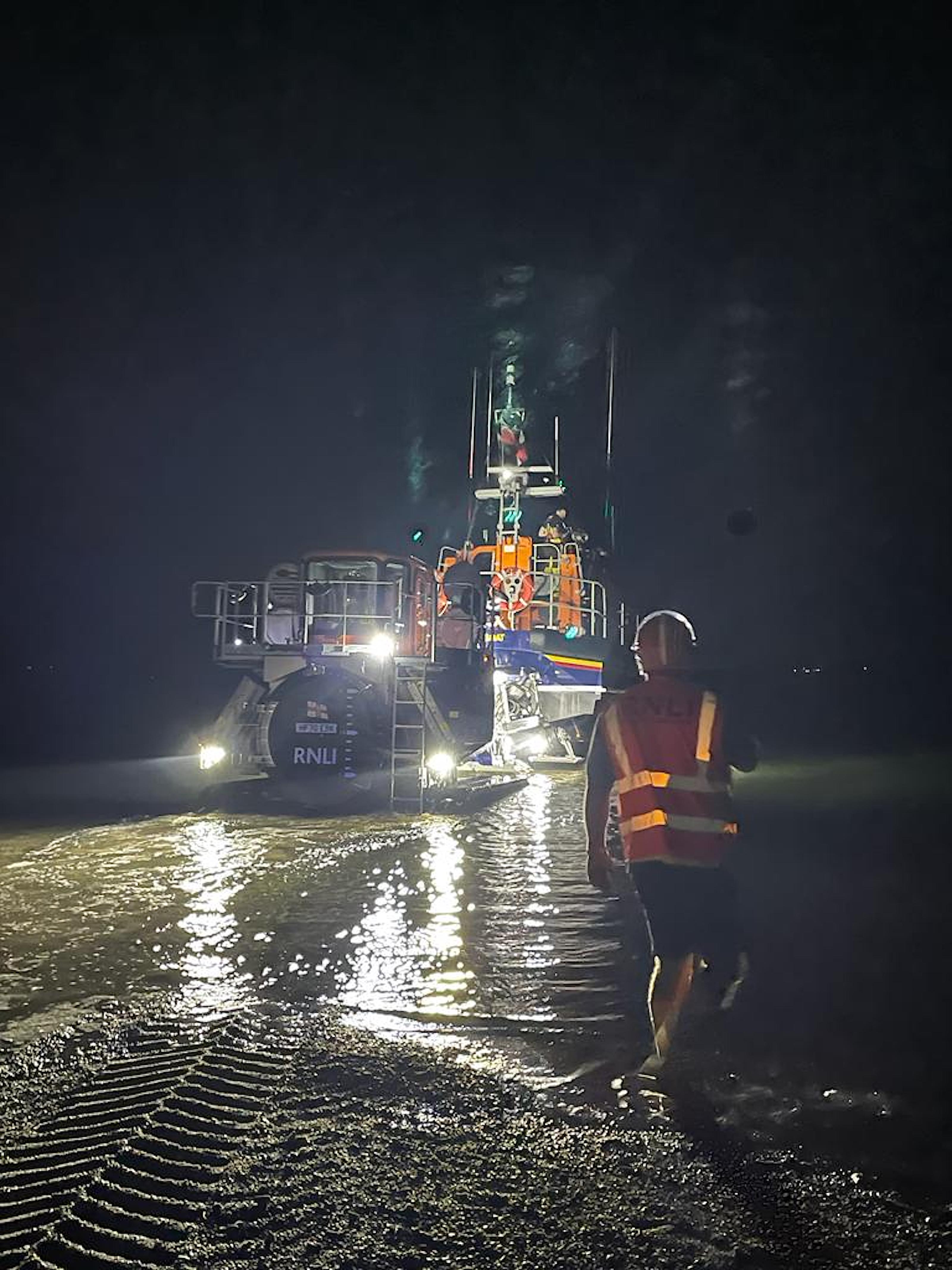 RNLI Pwllheli all-weather Shannon lifeboat launching at night in the dark with a shore crew member facing away from camera