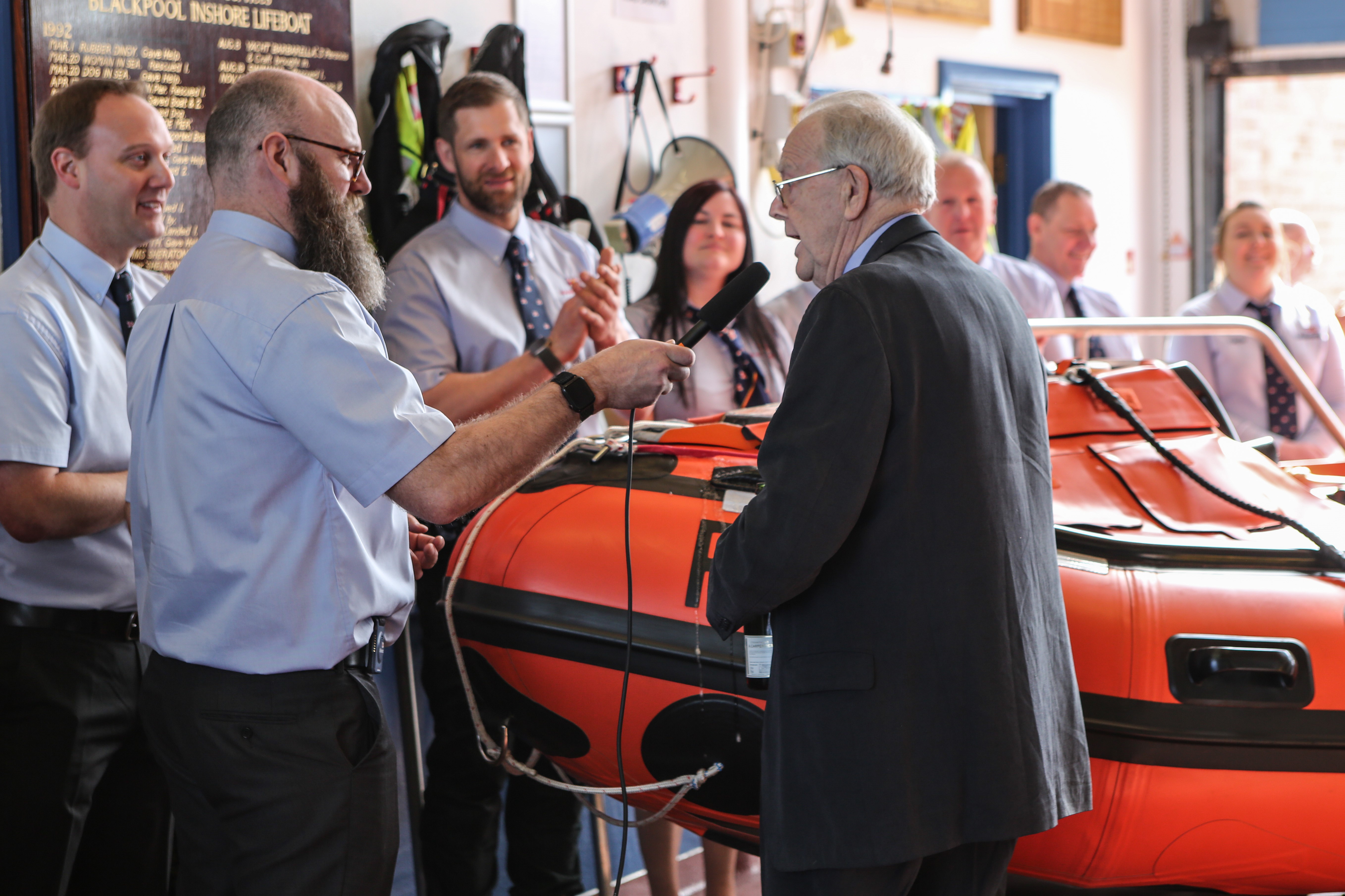 A man giving a speech in front of a lifeboat
