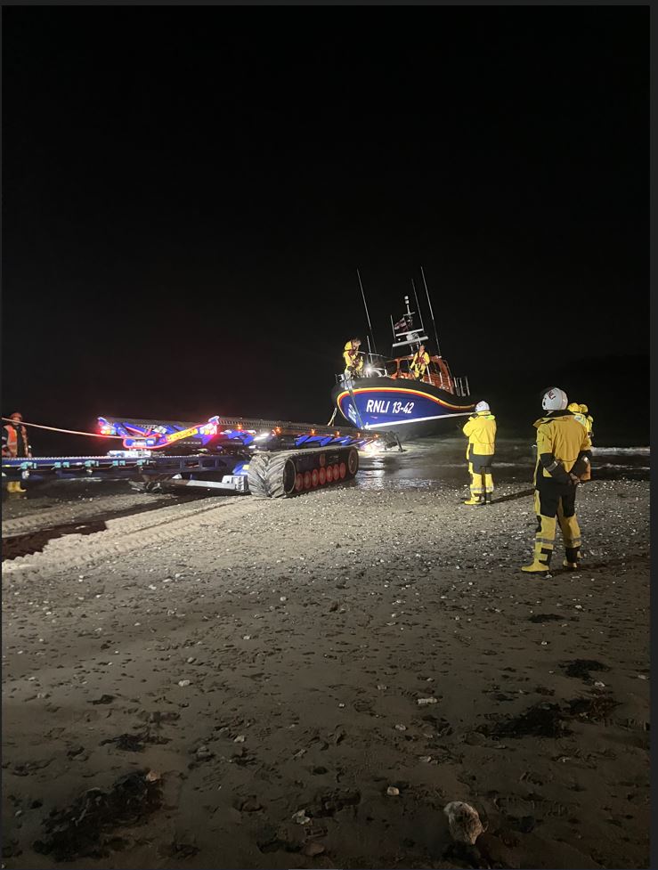Lifeboat and shore crew stood on the sand, the lifeboat is in the water ready to be pulled back onto the trailer