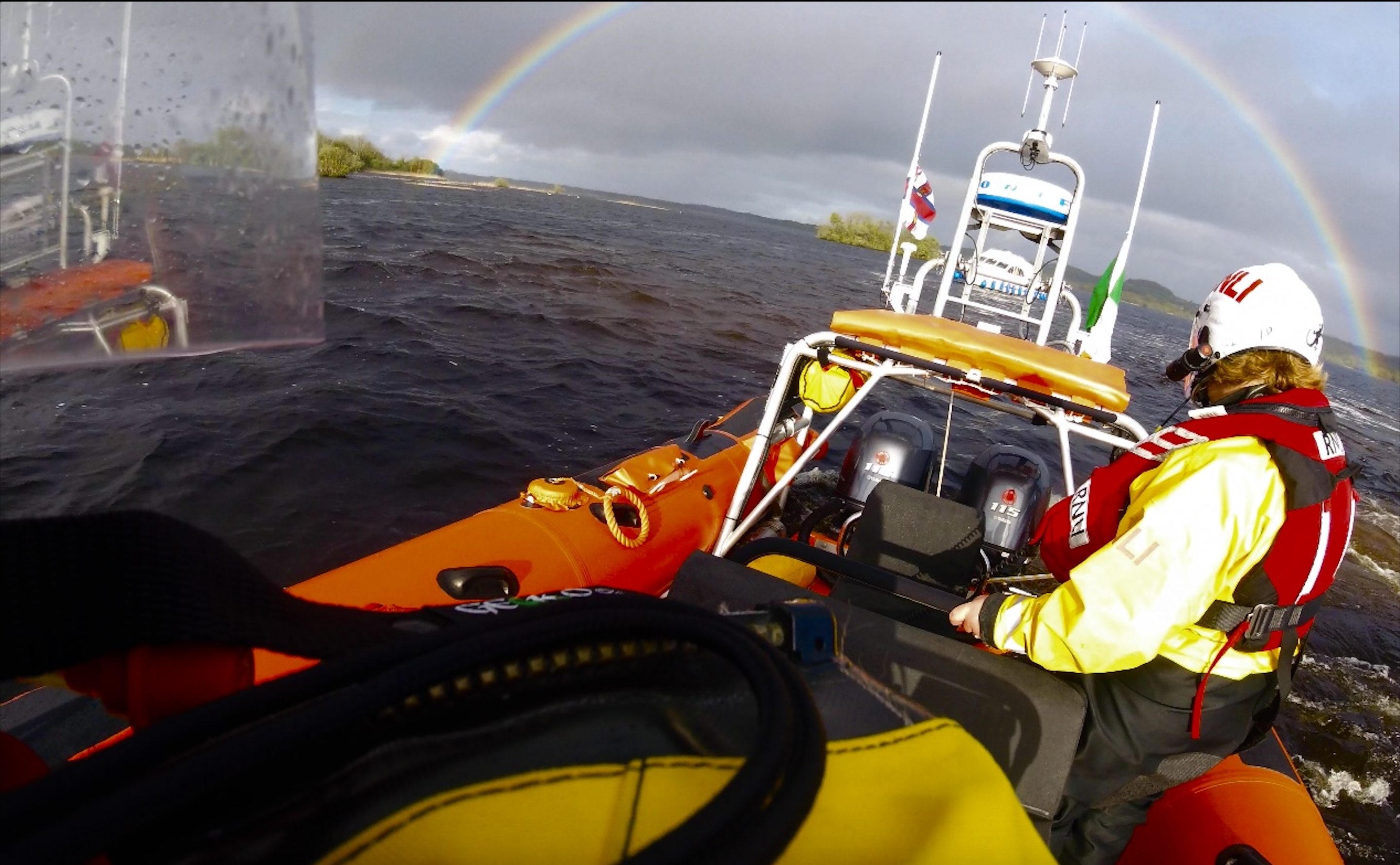 RNLI volunteers looking over the stern of the lifeboat to the casualty vessel, a rainbow encircles the casualty vessel