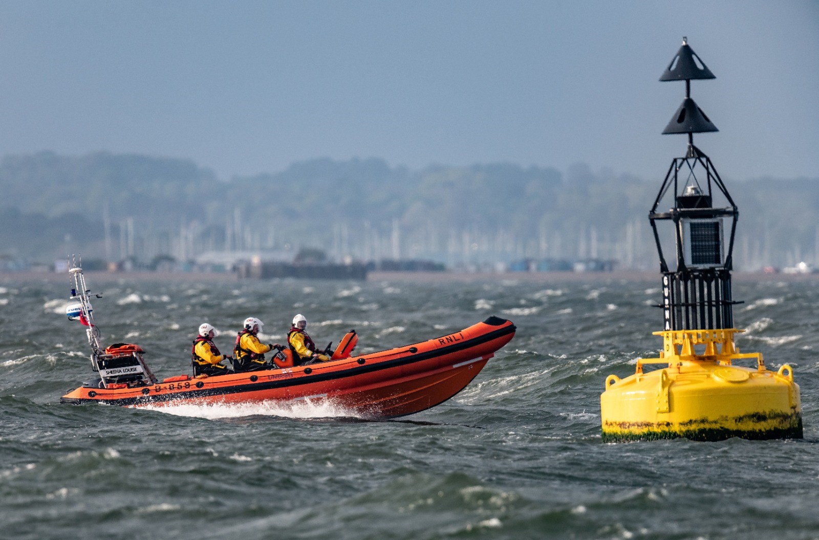 Stock photo of Cowes RNLI lifeboat at sea next to large yellow buoy.