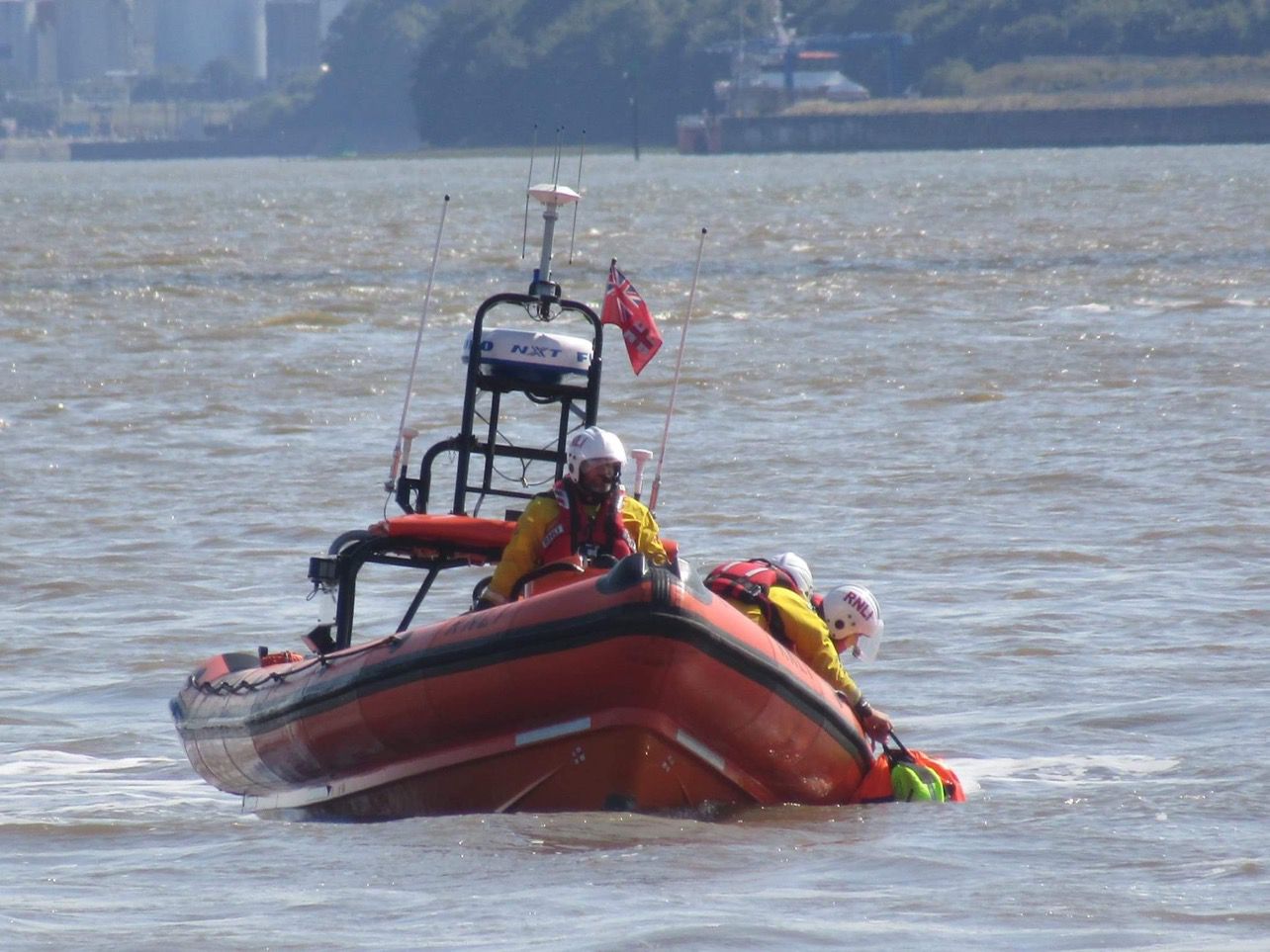New Brighton RNLI's Atlantic-85 lifeboat can be seen, bow toward the camera, on the water. To the right hand side, two crew are preparing to recover a training dummy aboard the boat.
