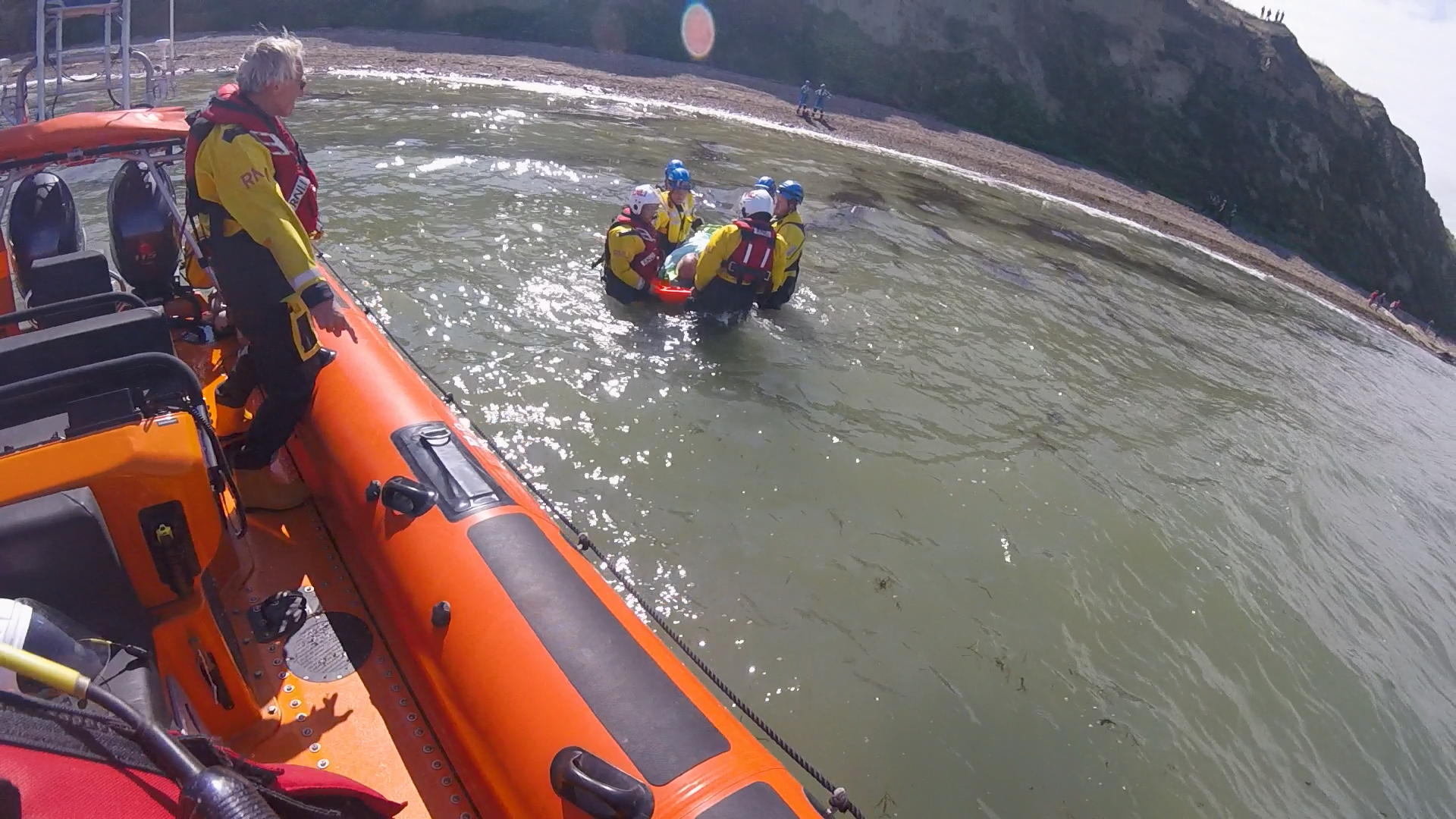 Lifeboat crew members assisted by coastguards bring the injured paraglider to the lifeboat