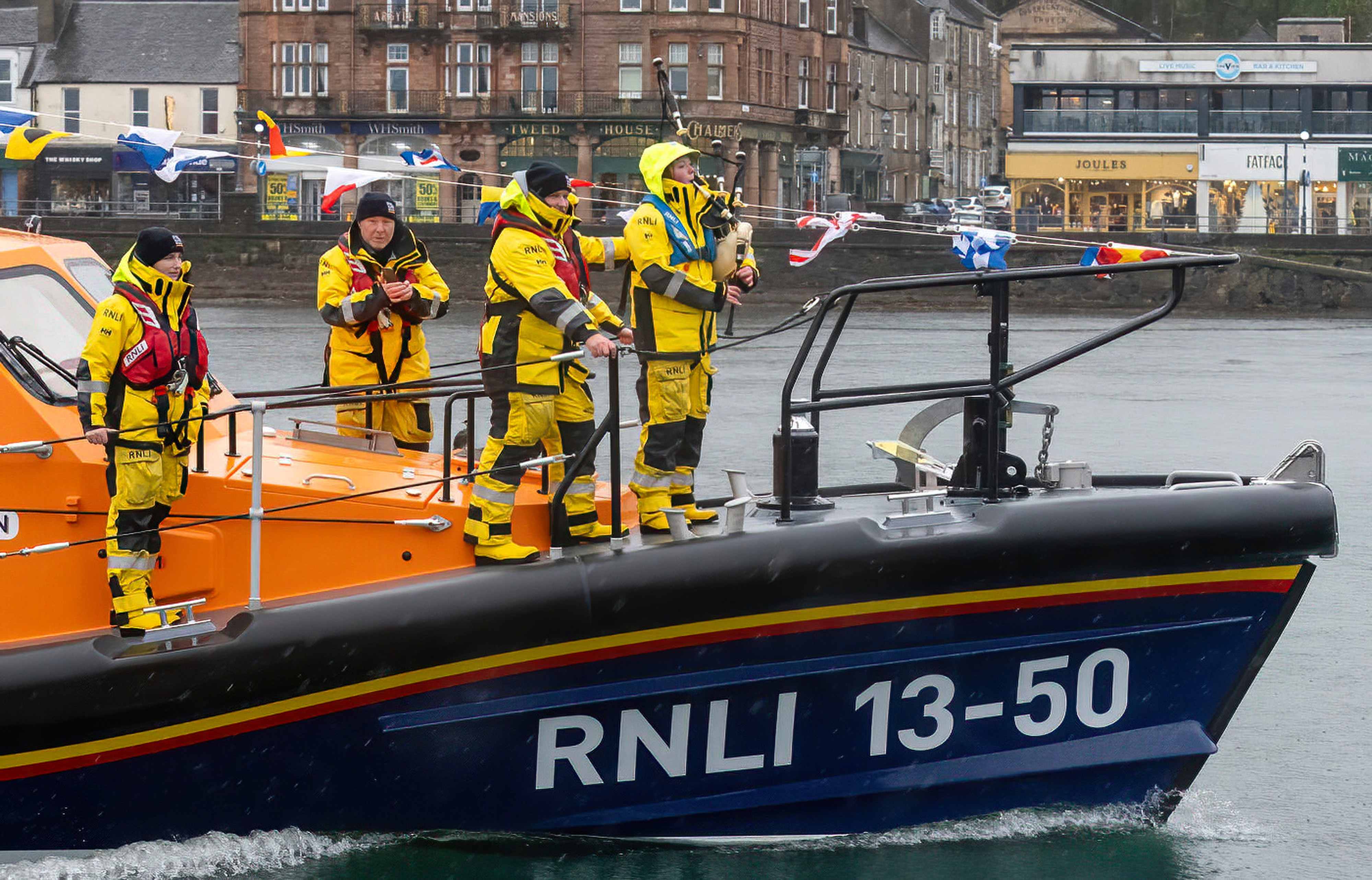 A piper is joined by members of the crew on the forward deck of the new lifeboat