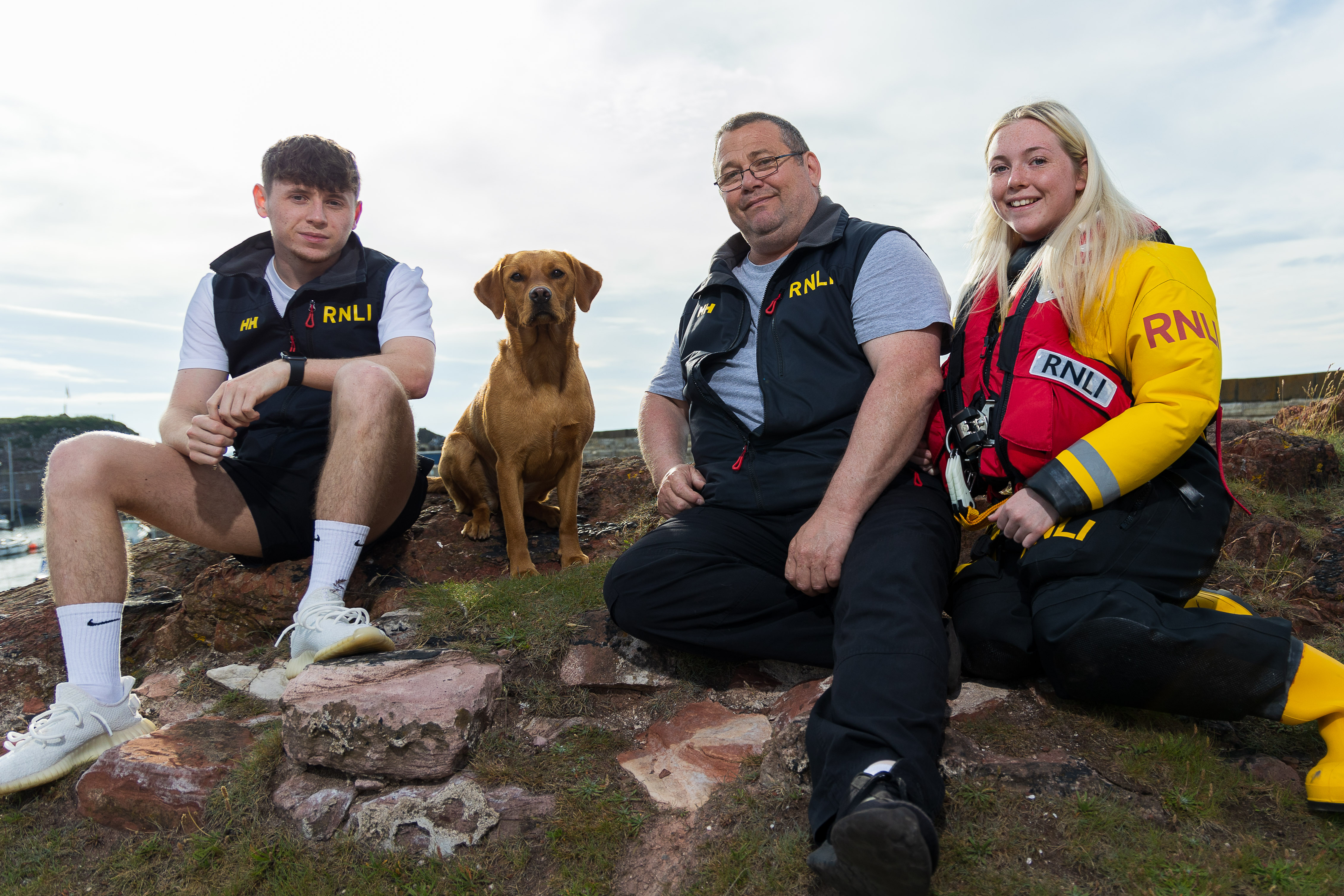 Photo shows three members of the same family sitting on rocks with their pet dog.