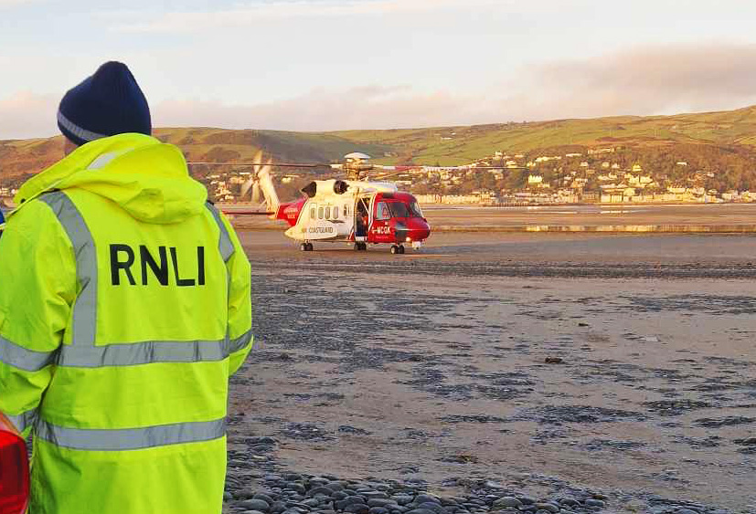RNLI volunteer in foreground and Coastguard helicopter in background on beach