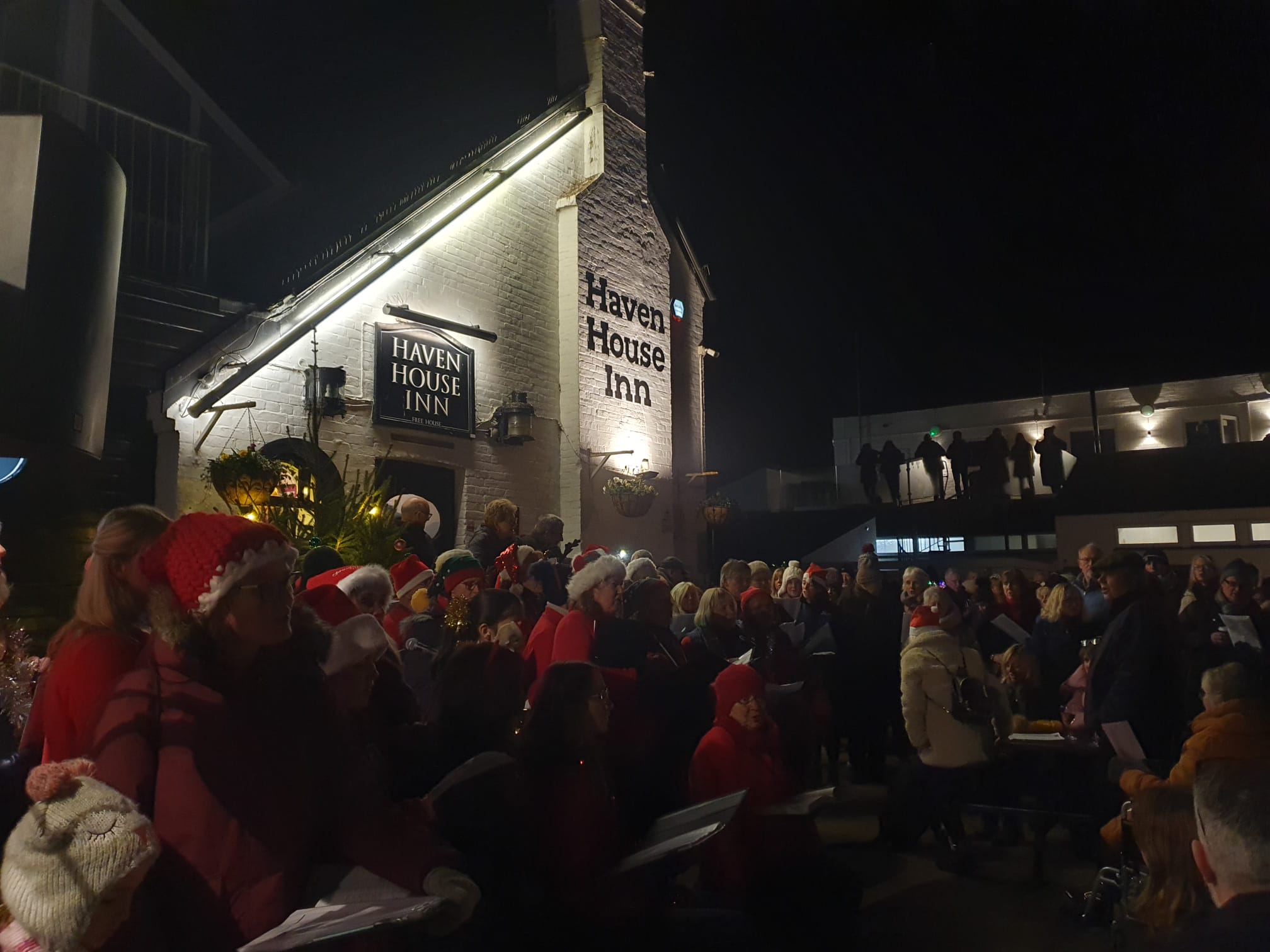 A group of choristers in Christmas hats singingoutside a white painted pub.