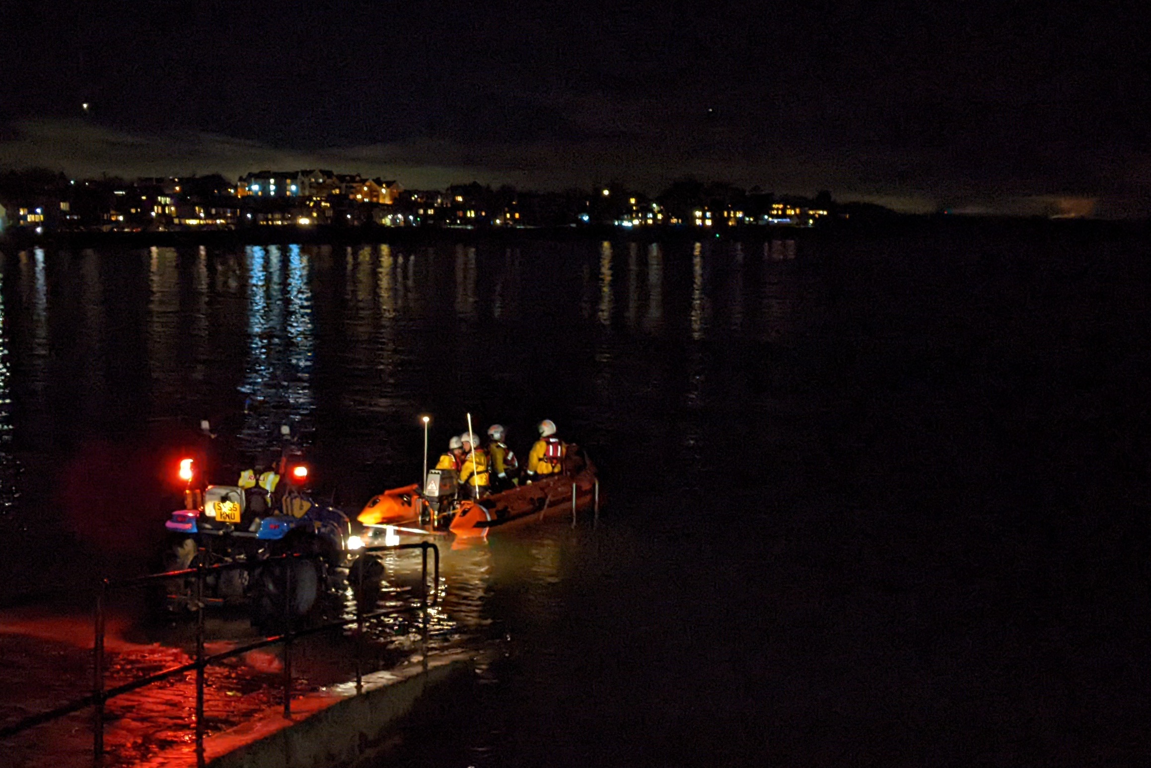 North Berwick RNLI launching at night, at high tide with tractor and lifeboat driving off trailer, town lights in the background