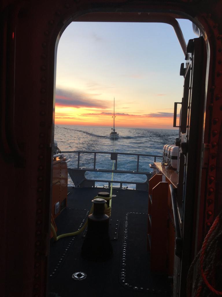 View, into the sunset, through the wheelhouse door, of the casualty yacht being towed home by the lifeboat