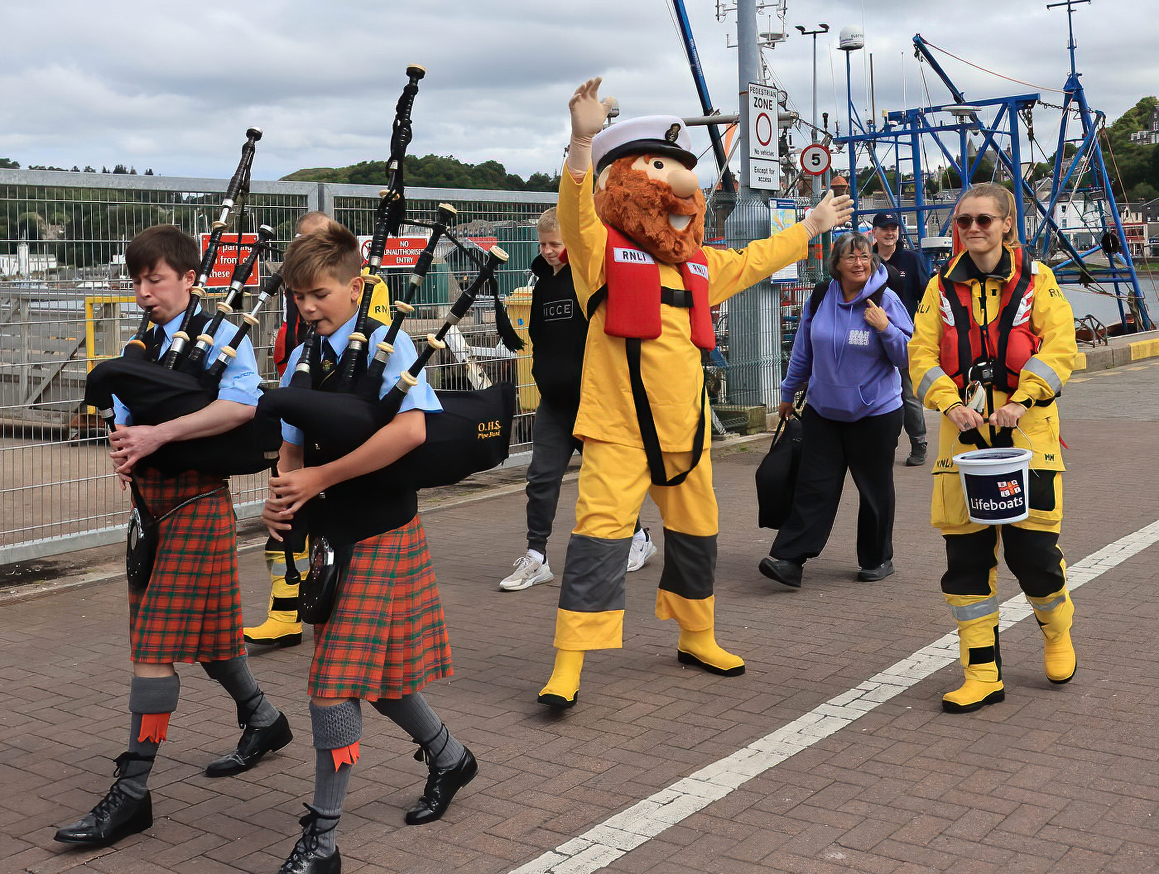 Mascot Stormy Stan is led by two young bagpipers along the middle pier towards the Open Day