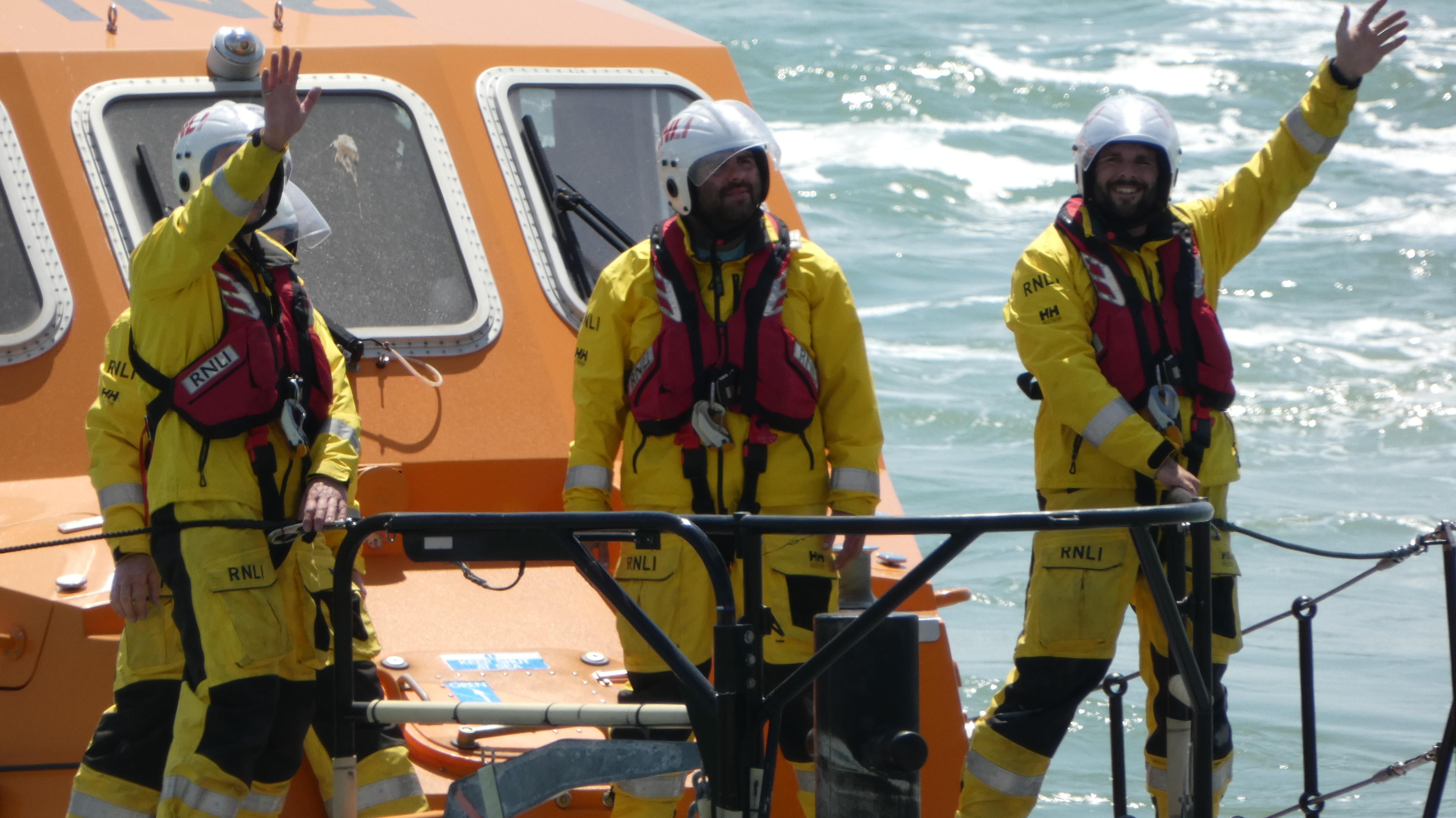 Three crew at front of lifeboat waving