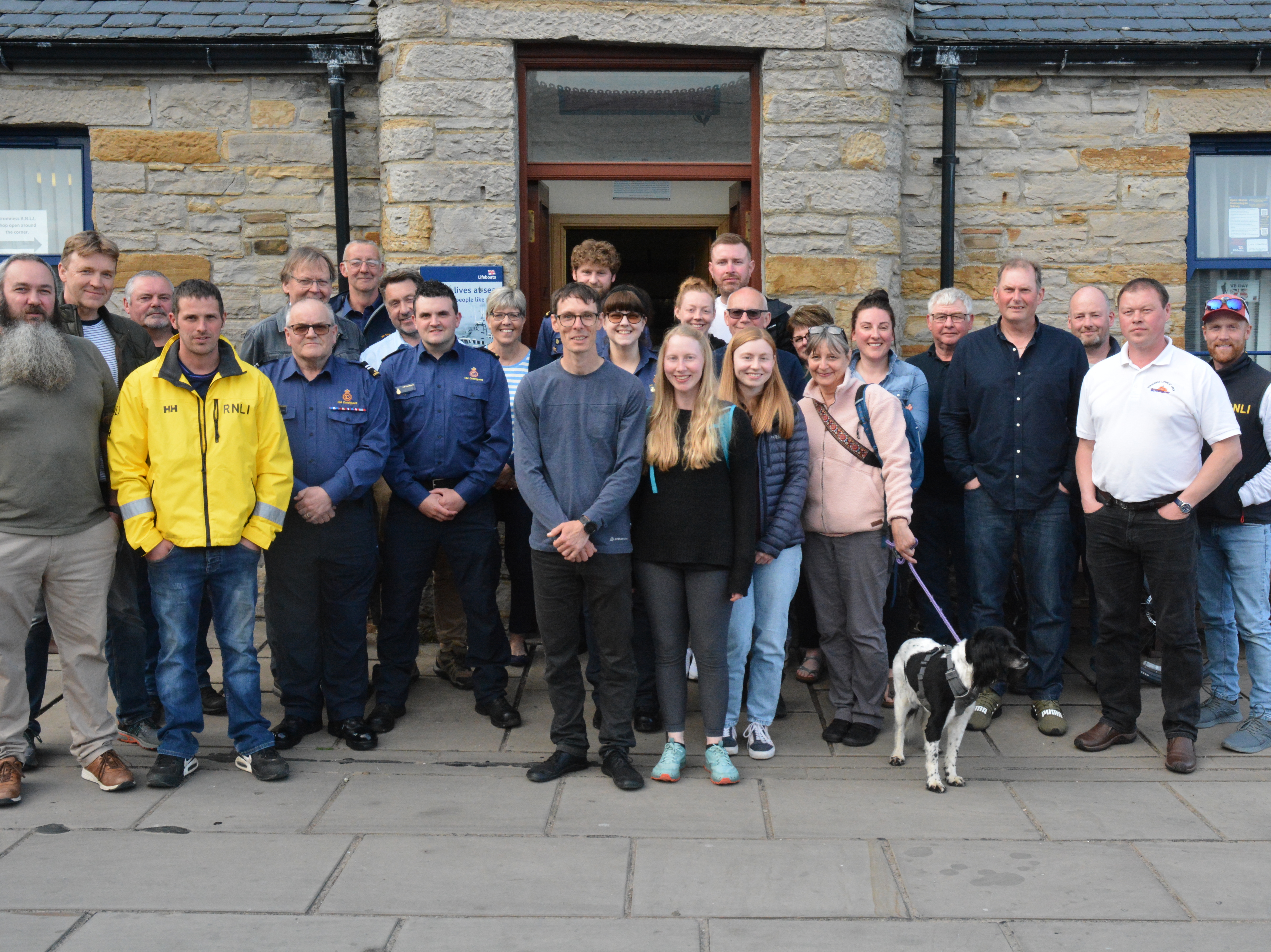 Large party of lifeboat folk grouped with casualty's family outside lifeboat station