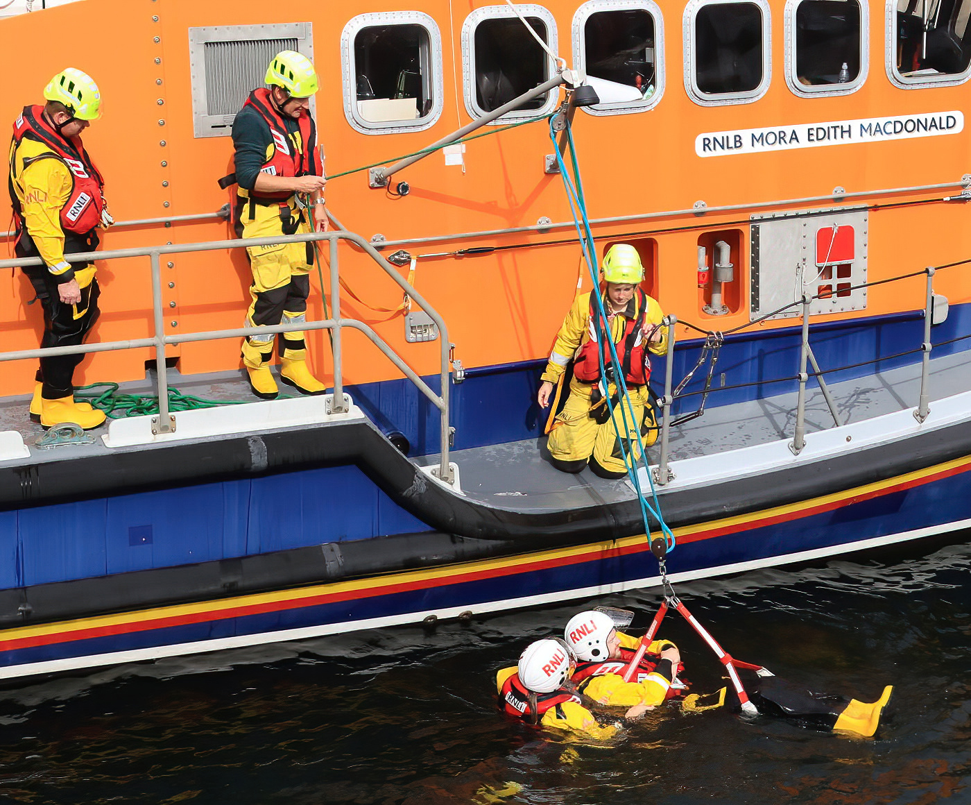 A photo of five crew members in their yellows, to of them in the water, using winching equipment to lift each other safely from the sea.