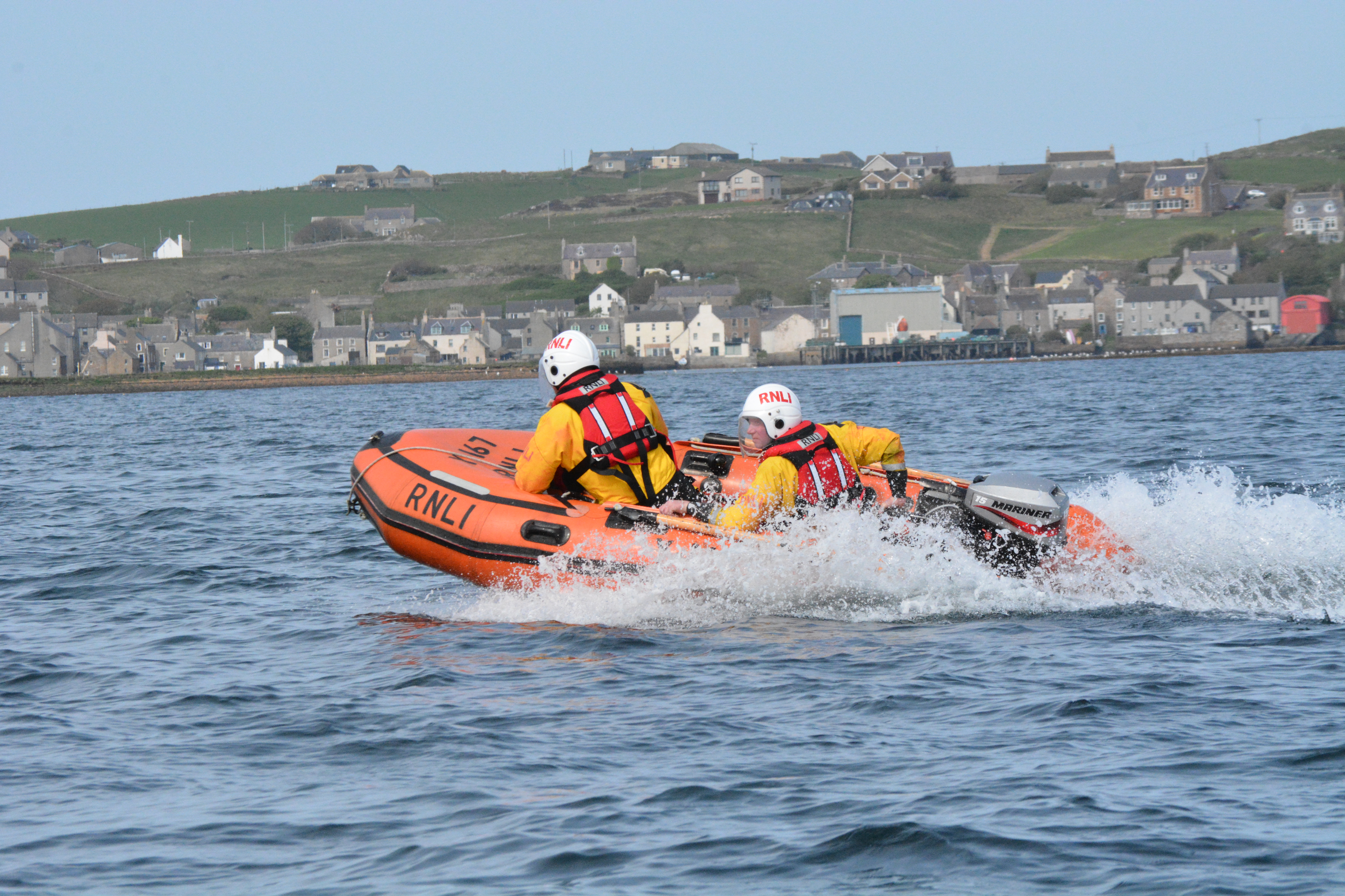 Two, yellow-clad volunteers, wearing white helmets operating a small RIB in the harbour