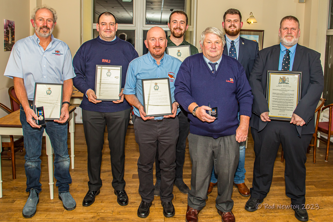 Seven crew members with their framed commendations and medals.