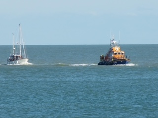 A lifeboat towing a sailing yacht. 