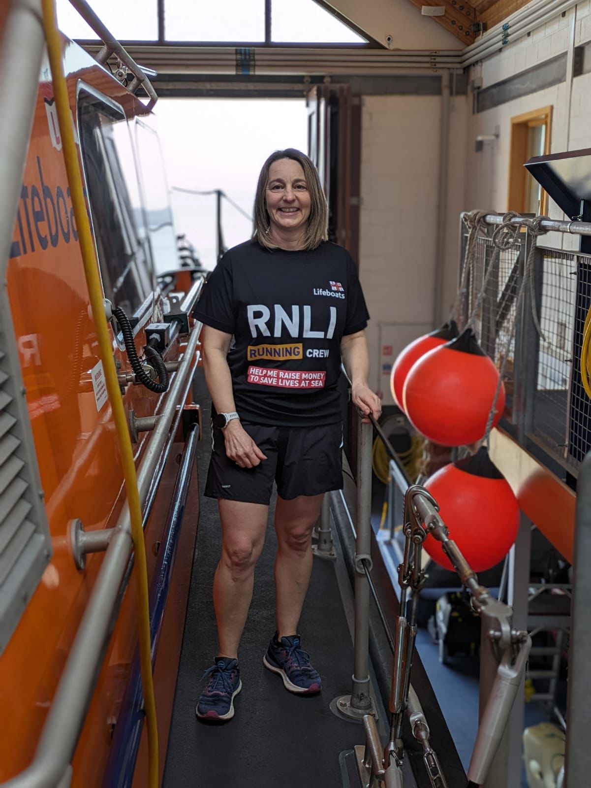 Lady in running clothing, standing beside railing of the RNLI lifeboat within lifeboat station