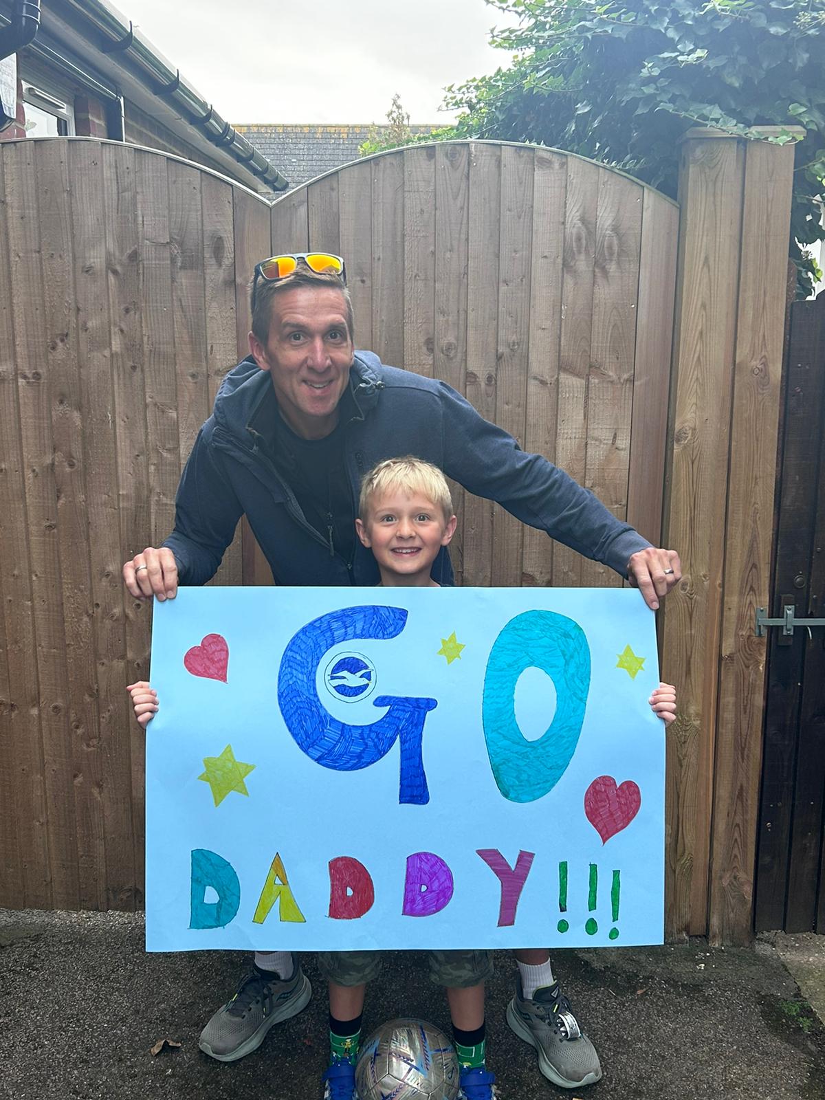 A man stood with a young boy holding a large paper sign reading 'Go Daddy!!!'.