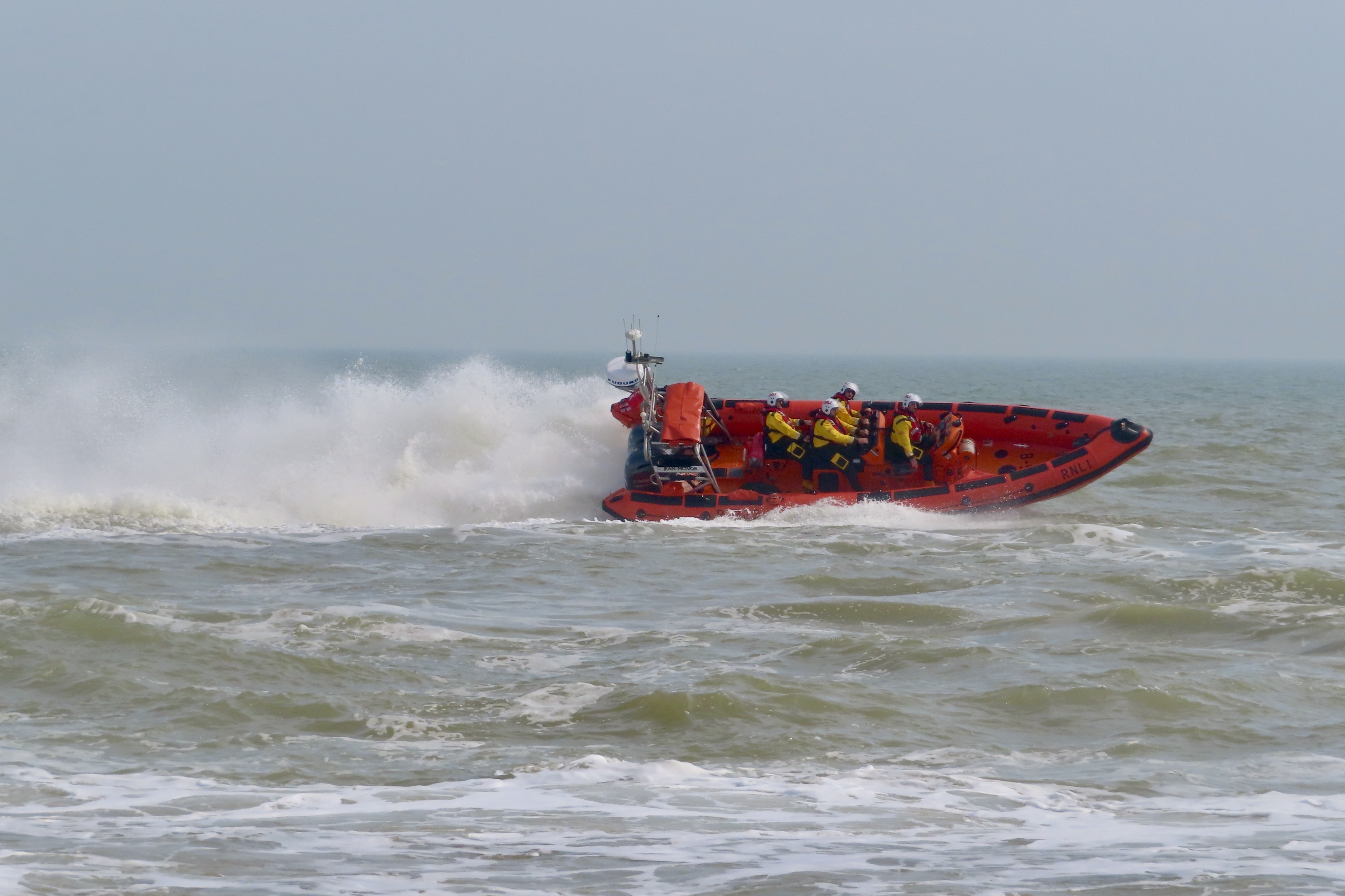 A spectacular picture of the Littlestone RNLI Atlantic 85 lifeboat speeding across the water with surf thrown up behind it