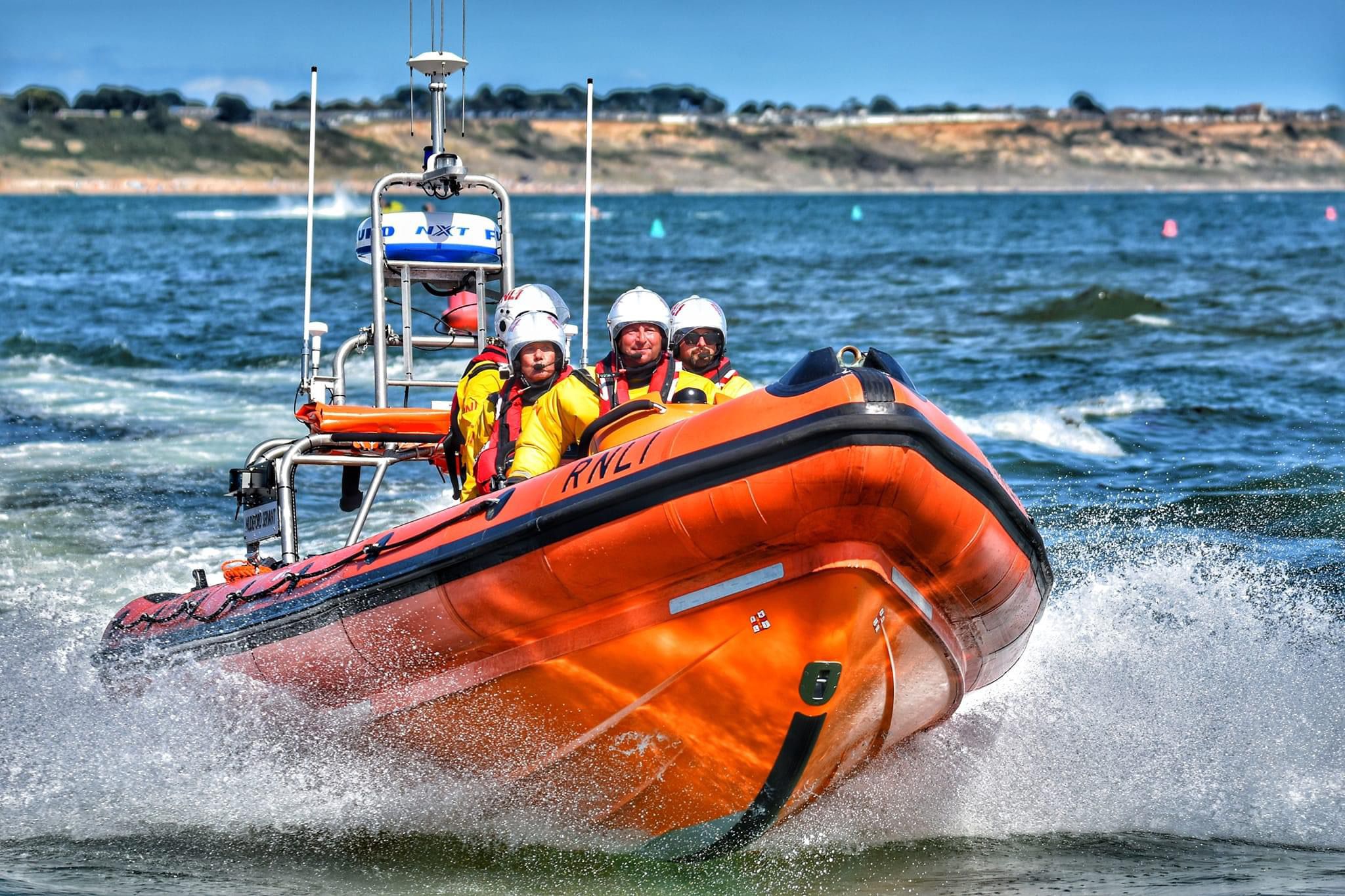 An orange RNLI rib with four crew speeding through the waves near Christchurch Harbour